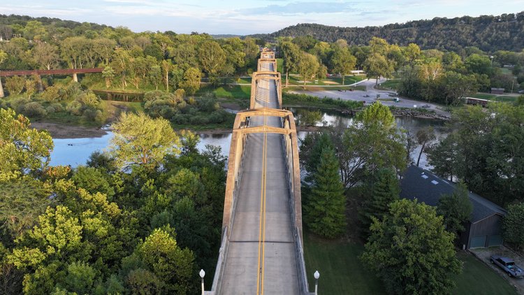 An aerial view capturing an impressive arch bridge traversing through a dense forest, showcasing the harmonious coexistence of infrastructure amidst natural beauty.