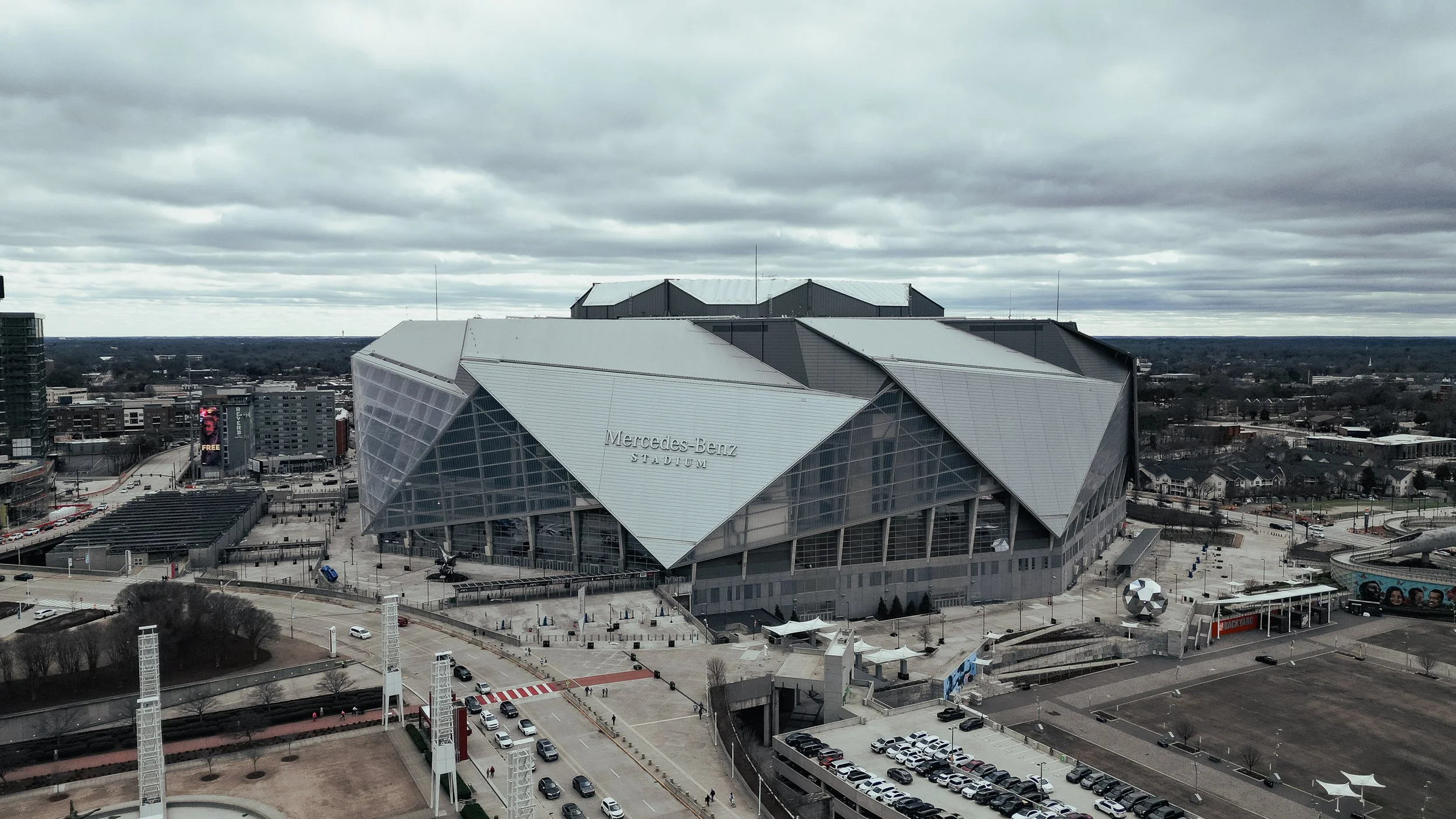 Aerial view of Mercedes-Benz Stadium in Atlanta, Georgia, on a cloudy day, showing the modern architecture and empty parking lot.