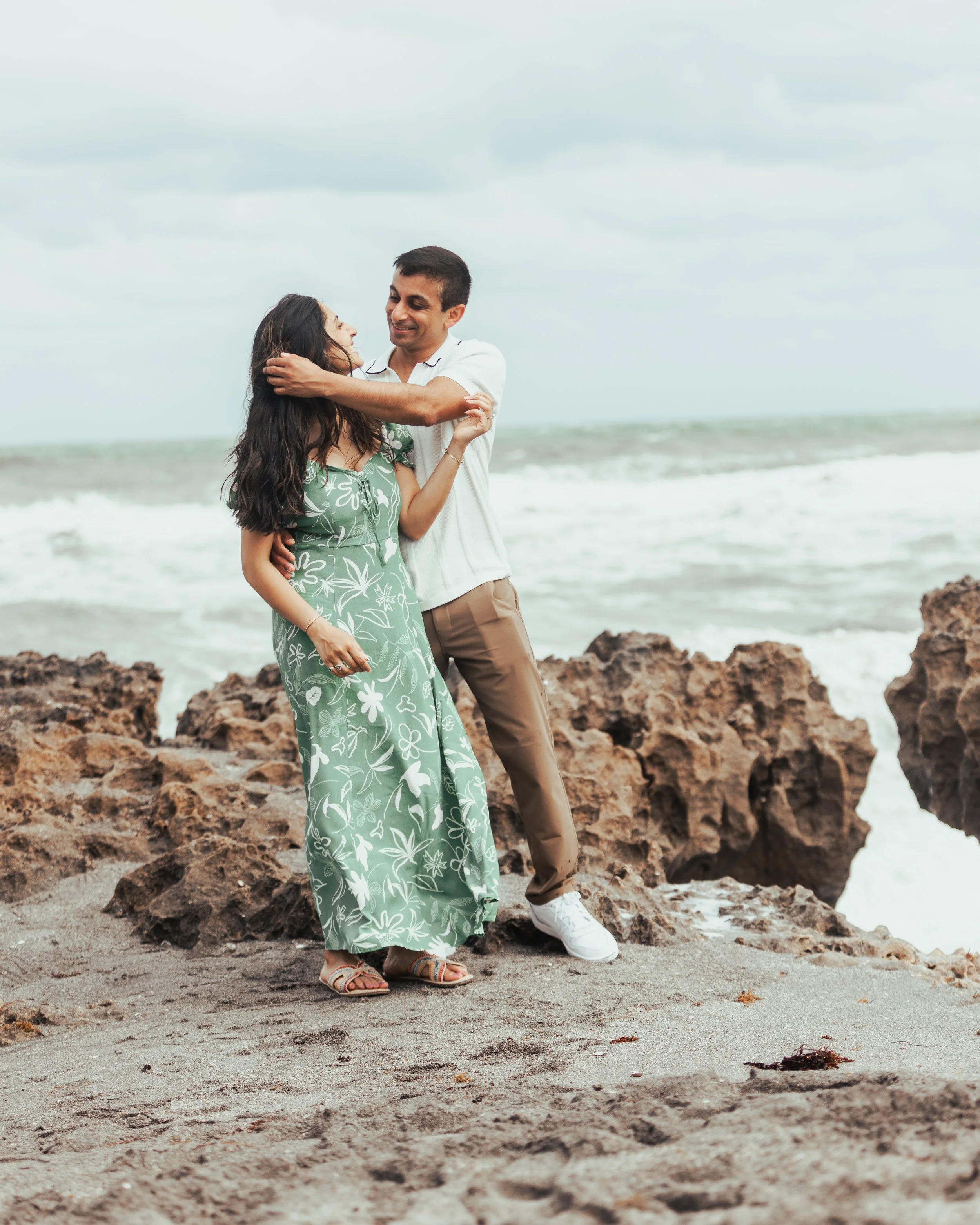A couple hugging on a rocky beach with the ocean in the background