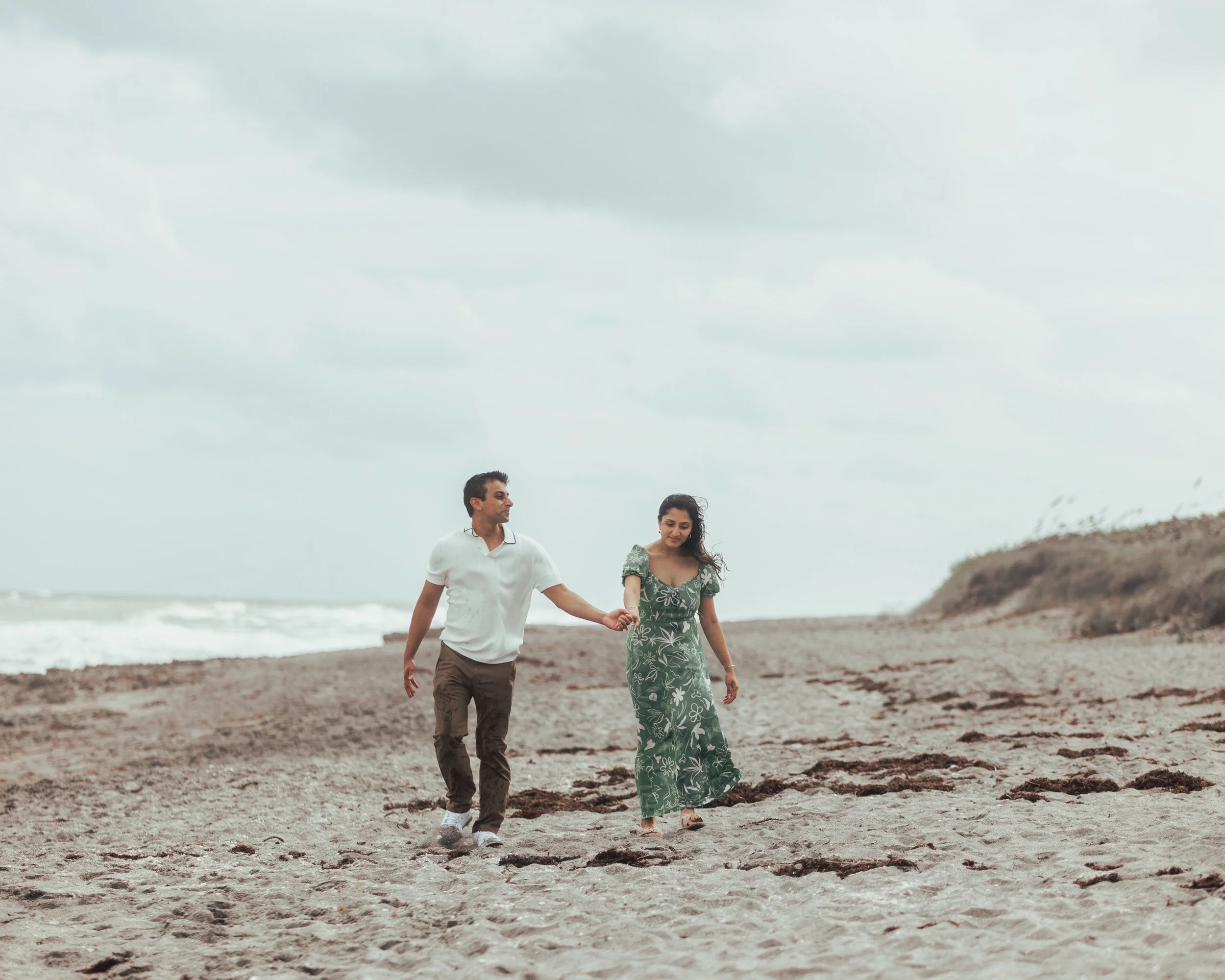 A man and woman walking hand in hand on a beach.