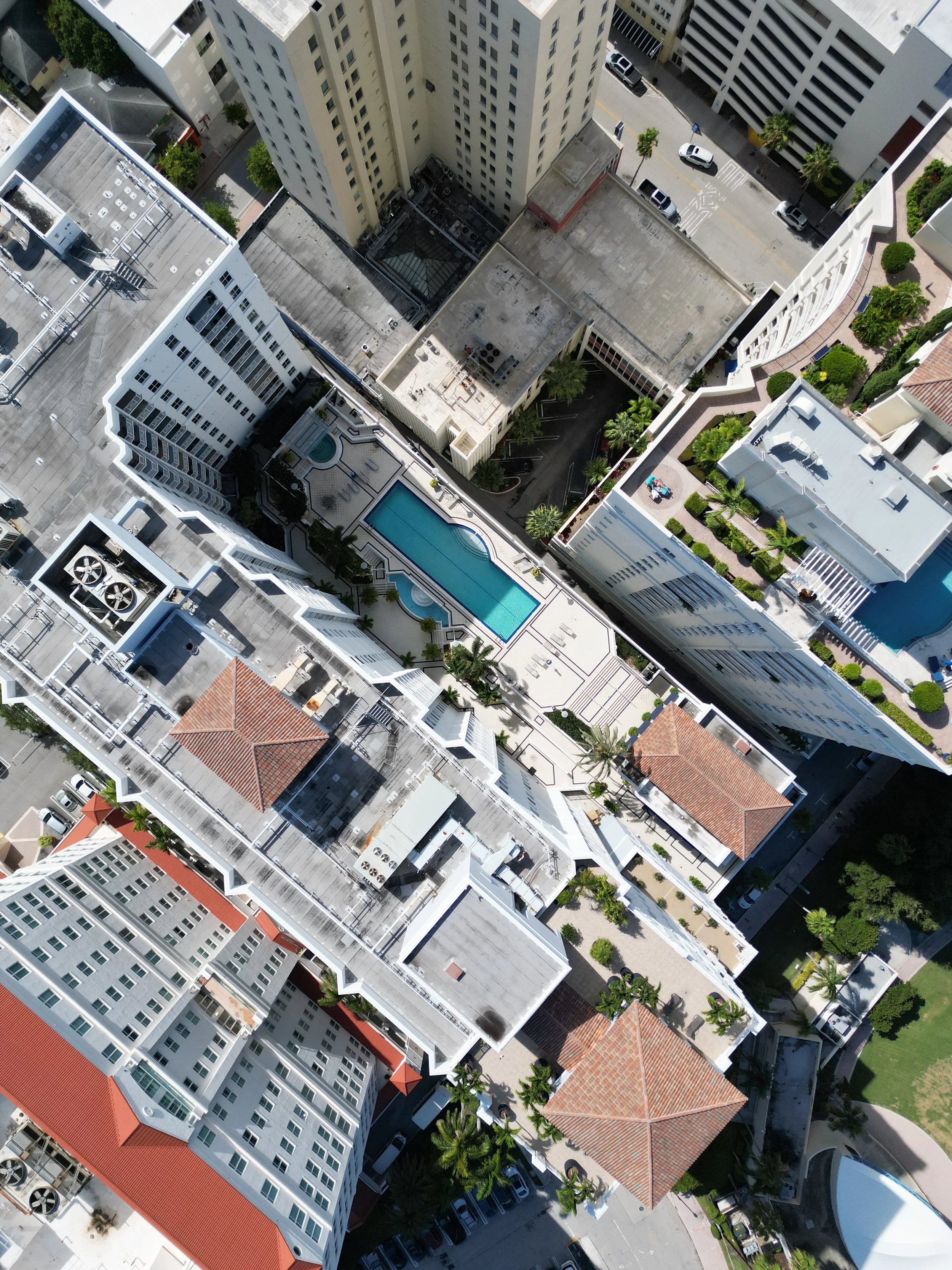 Aerial view of a city block with tall buildings, swimming pools, and streets lined with cars and palm trees.