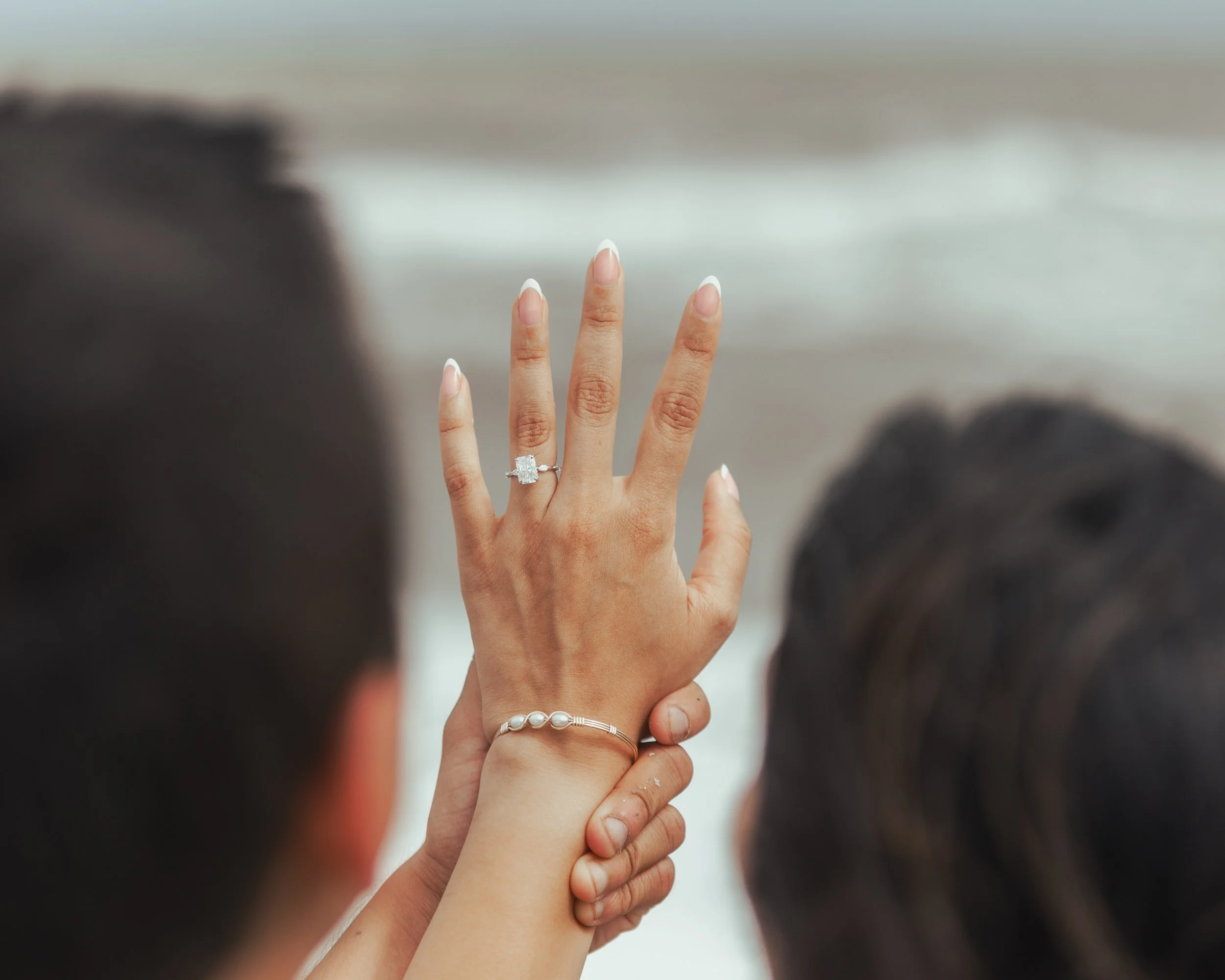 A woman showing a ring on her wedding finger during a beach wedding ceremony, with a person's hand holding her hand.