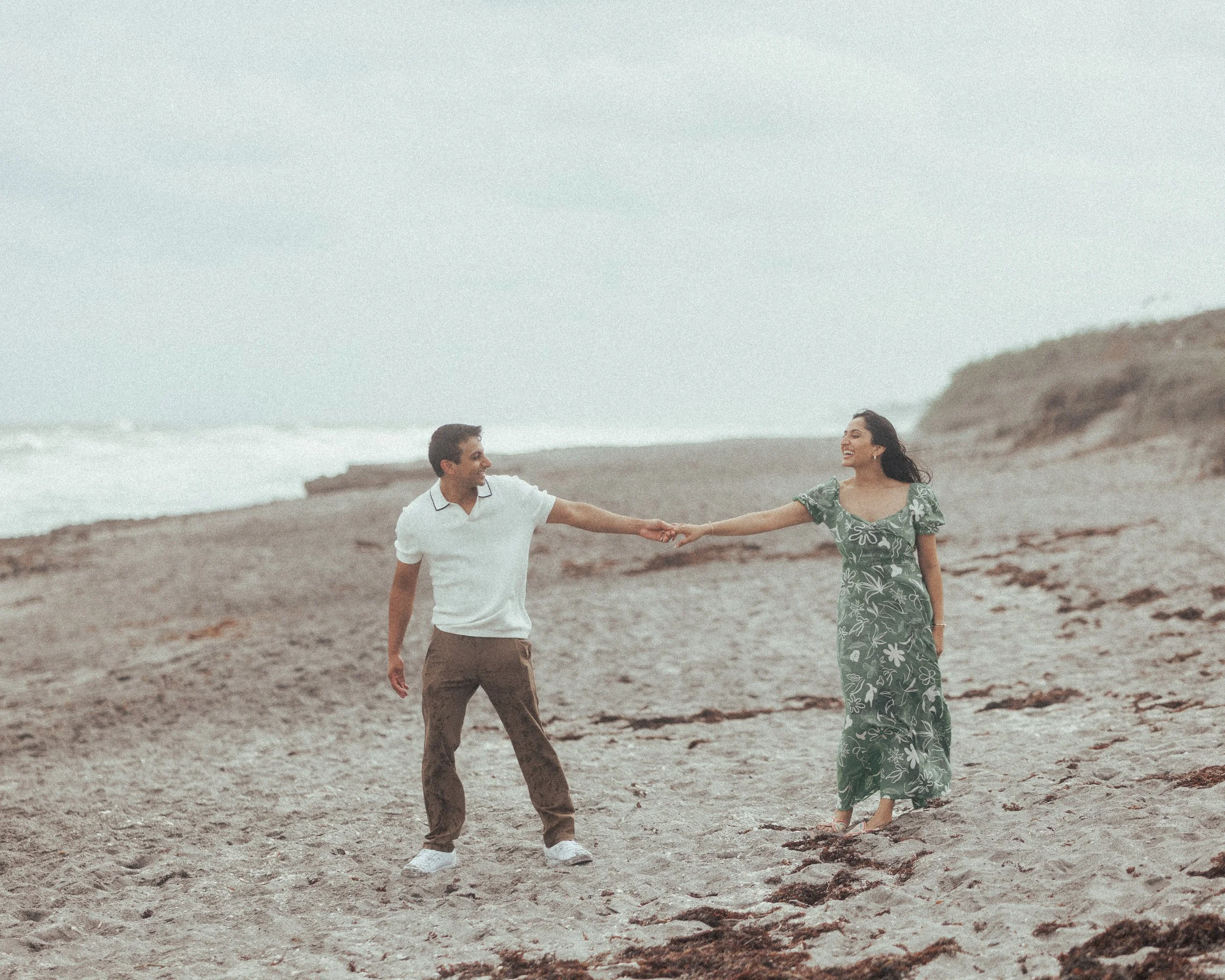 A man and a woman holding hands on a beach, smiling and enjoying their time together.