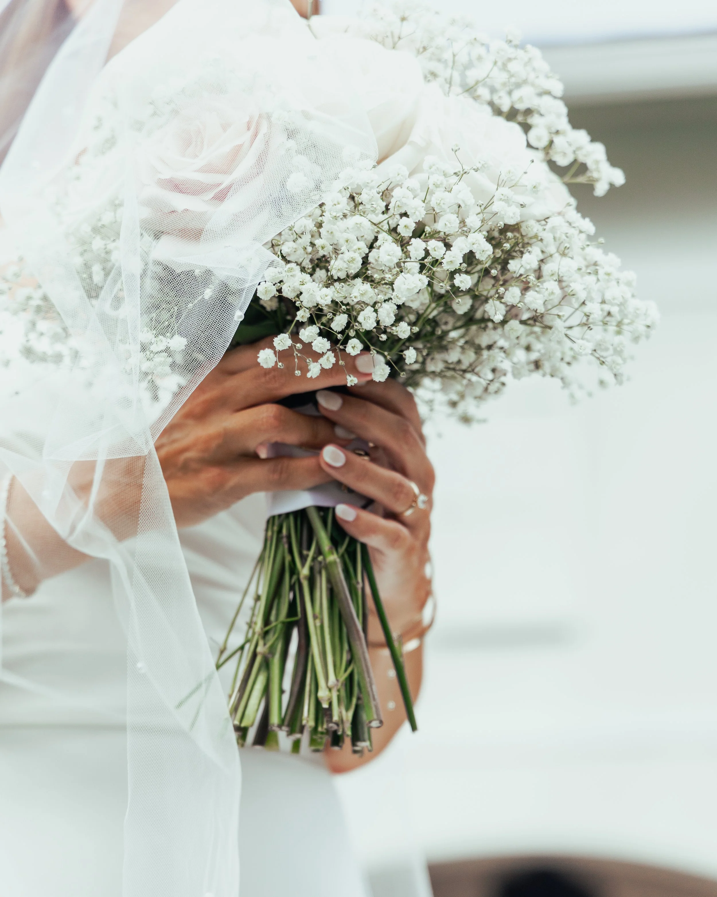 Bride holding a bouquet of white baby's breath flowers with a sheer veil over her shoulder on her wedding day.