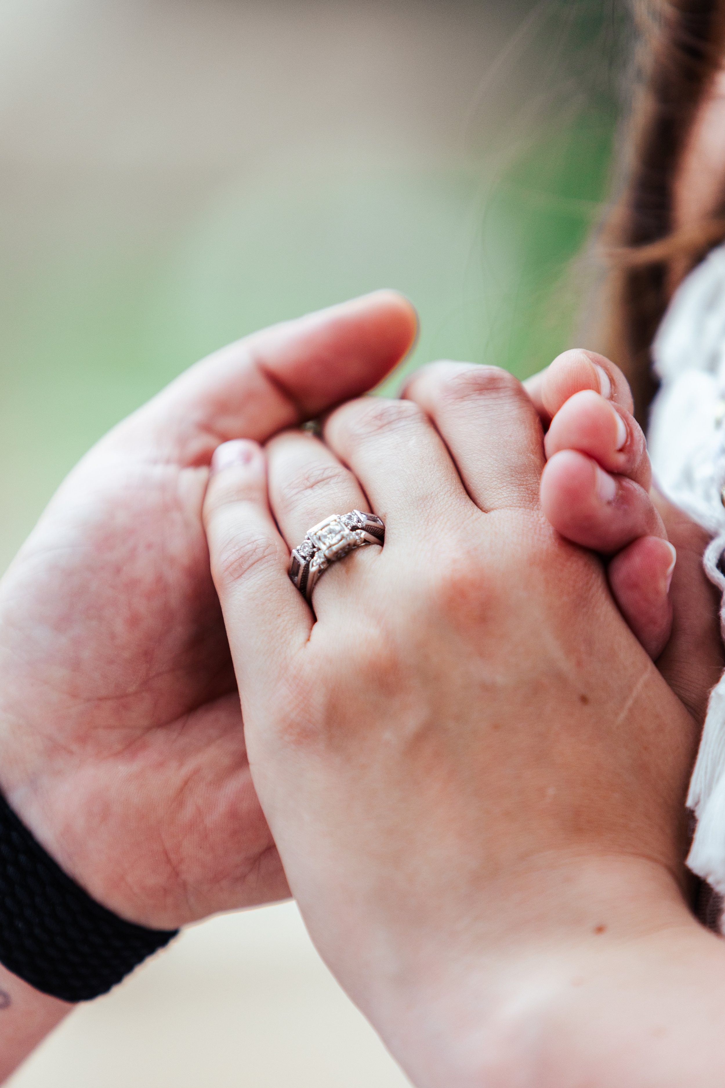 Close-up of two hands clasped, showing a wedding ring on the ring finger of one hand.