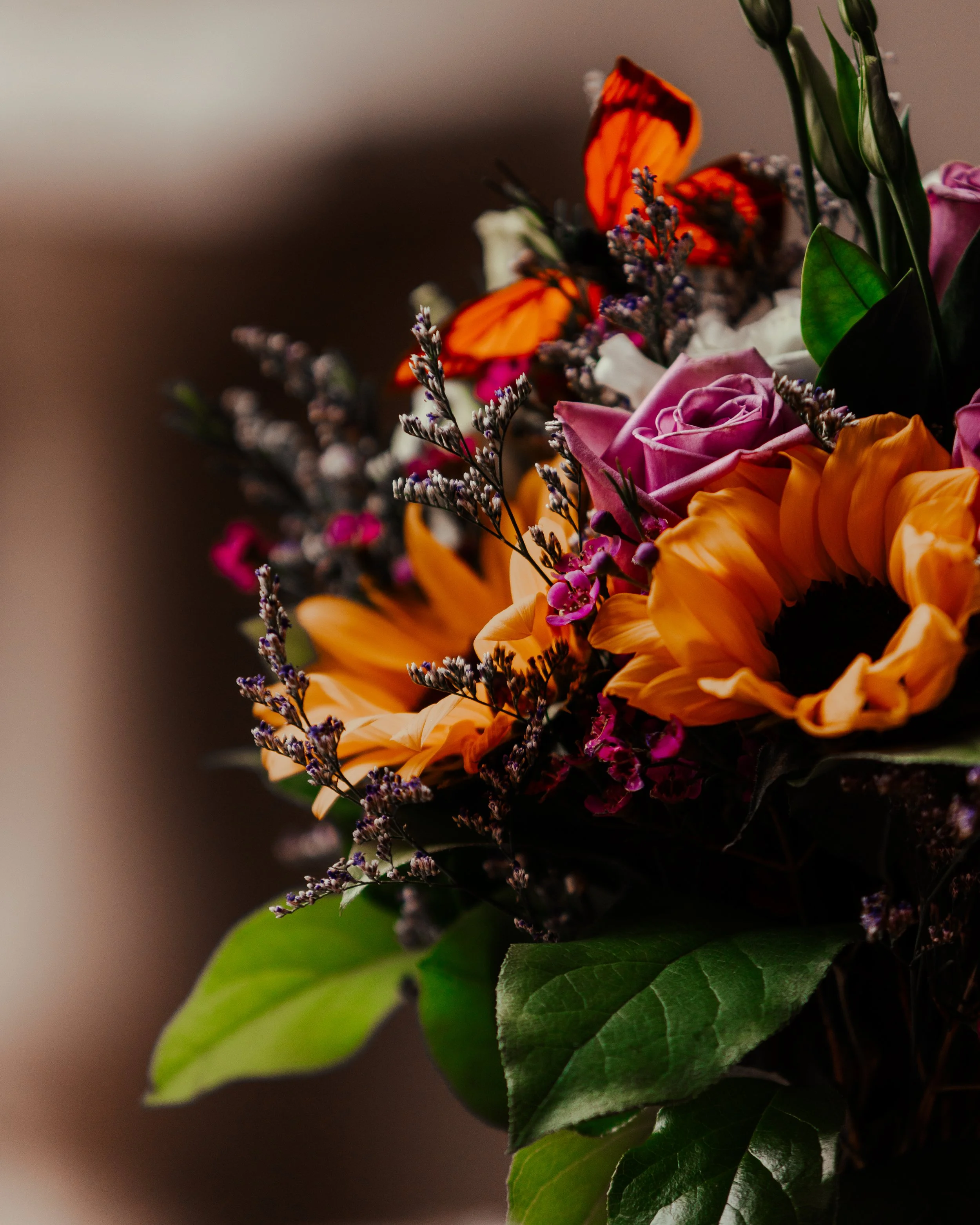 A colorful bouquet of flowers including sunflowers, pink roses, purple flowers, and orange butterflies.