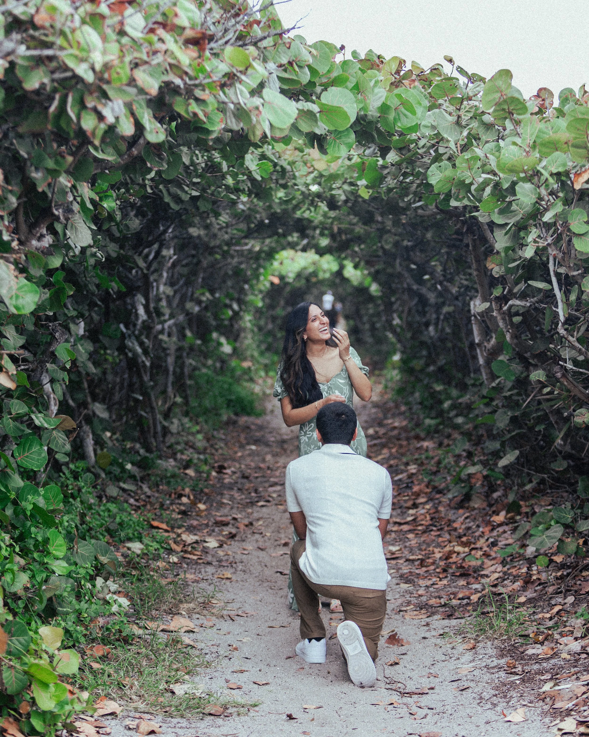 A man on one knee proposing to a woman in a leafy tunnel.