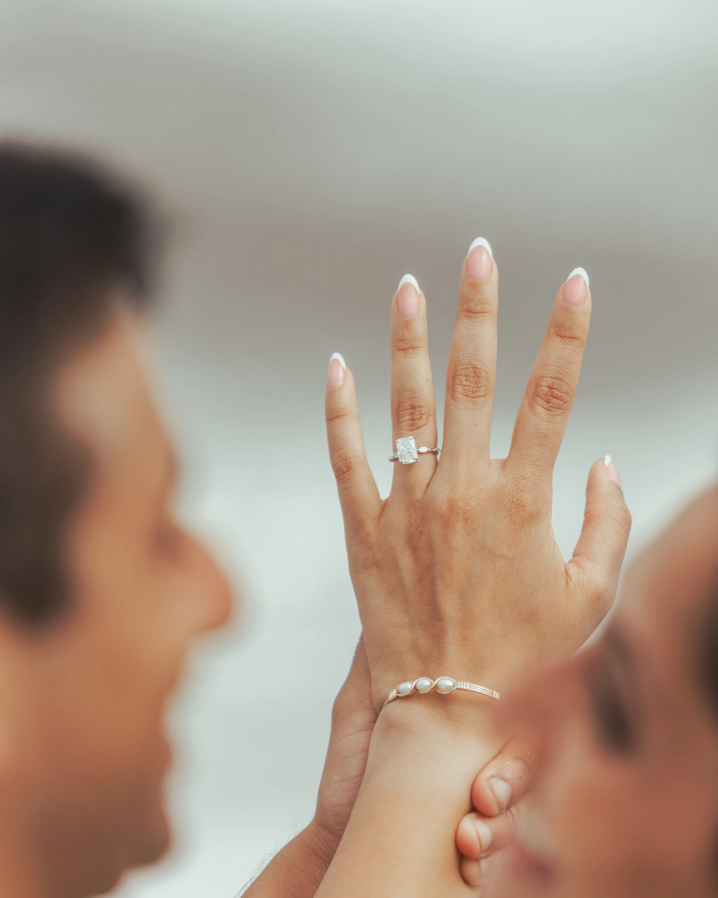 A person is showing their hand with an engagement ring and a bracelet, while another person is holding their hand from below.