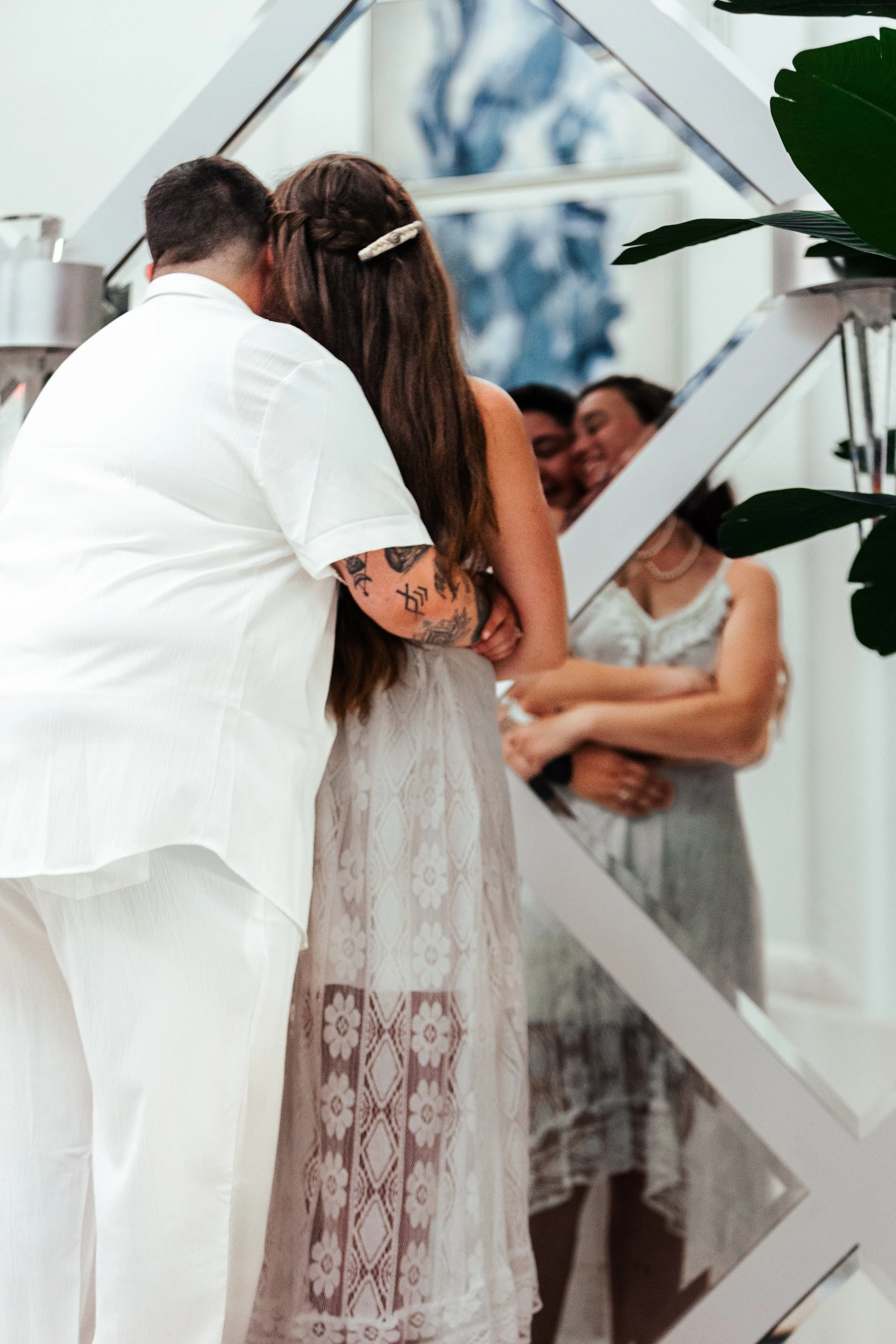 People embracing in front of a large mirror at a social gathering.