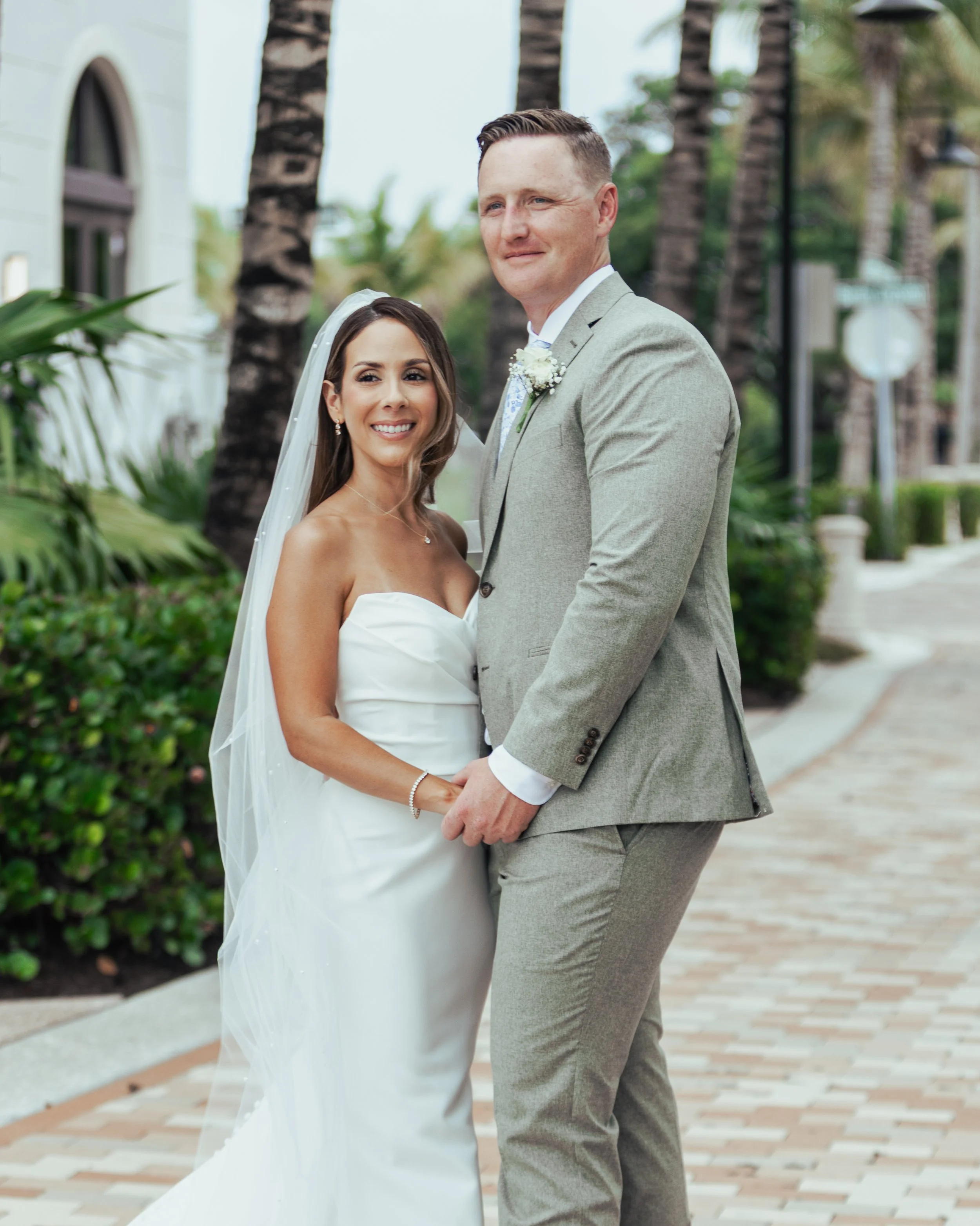 A bride and groom pose for a photo outdoors during their wedding, holding hands and smiling.