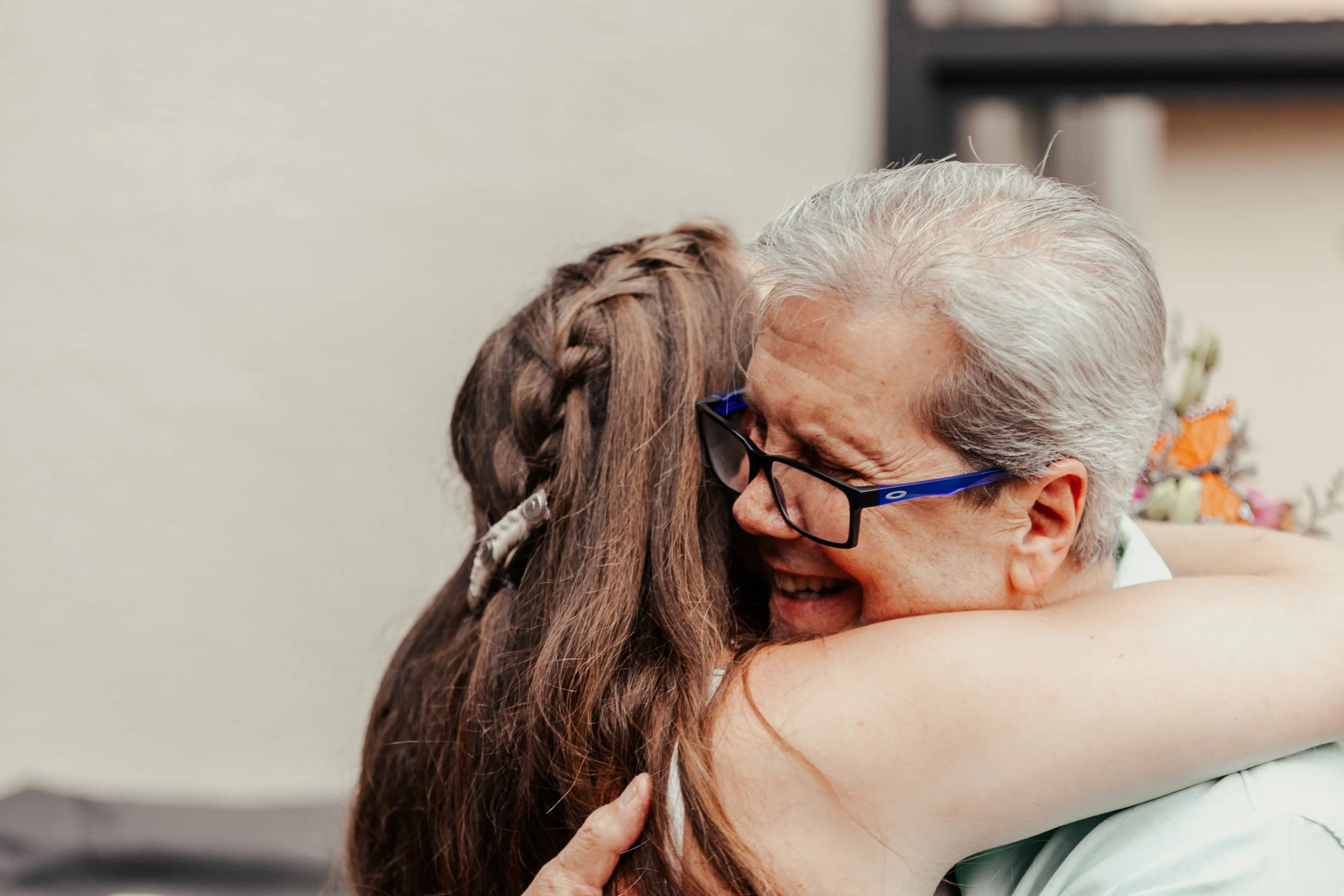 An elderly man with gray hair and glasses hugging a young girl with braided hair.