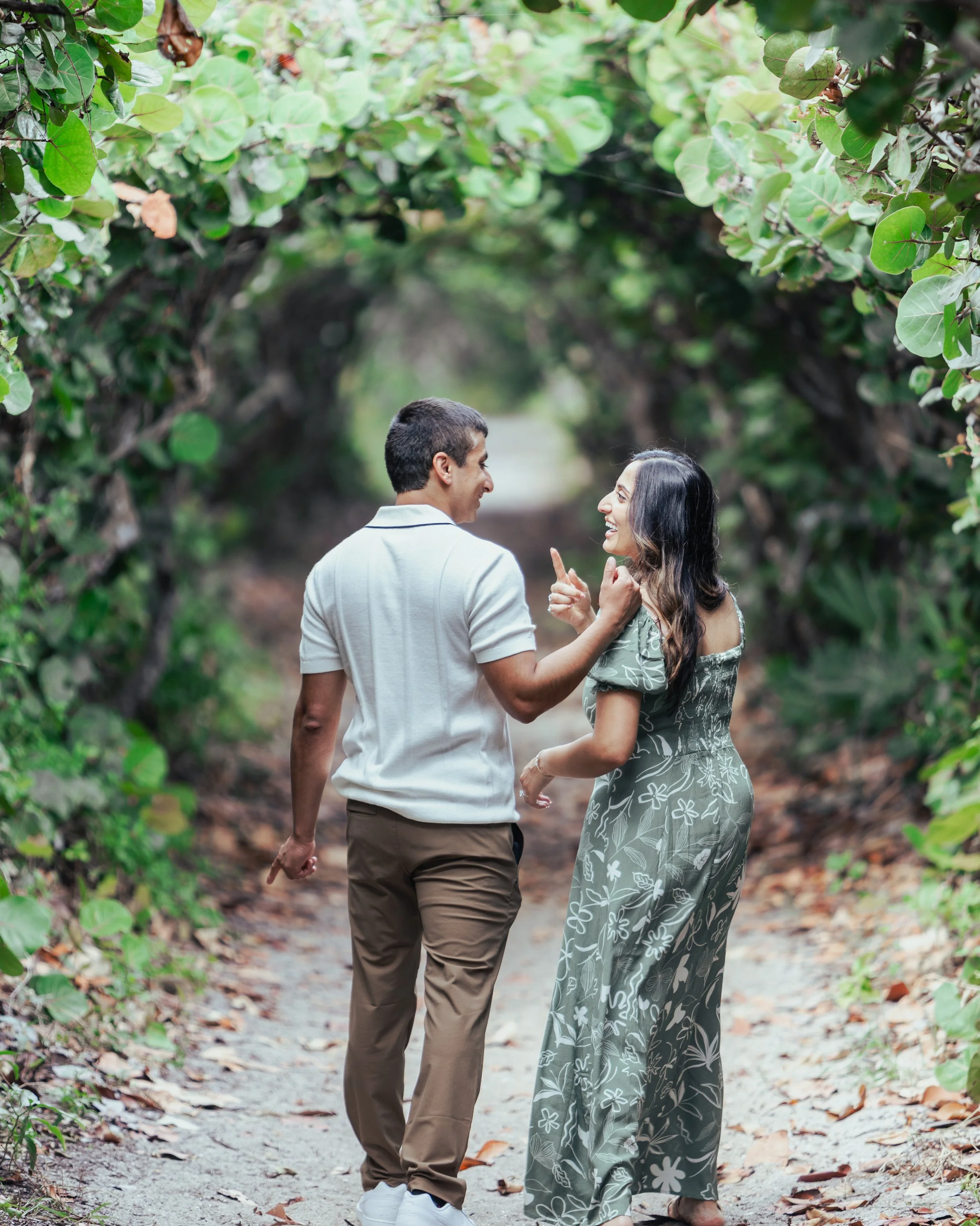 A couple walking through a lush, green, covered tunnel of trees, smiling and enjoying each other's company.