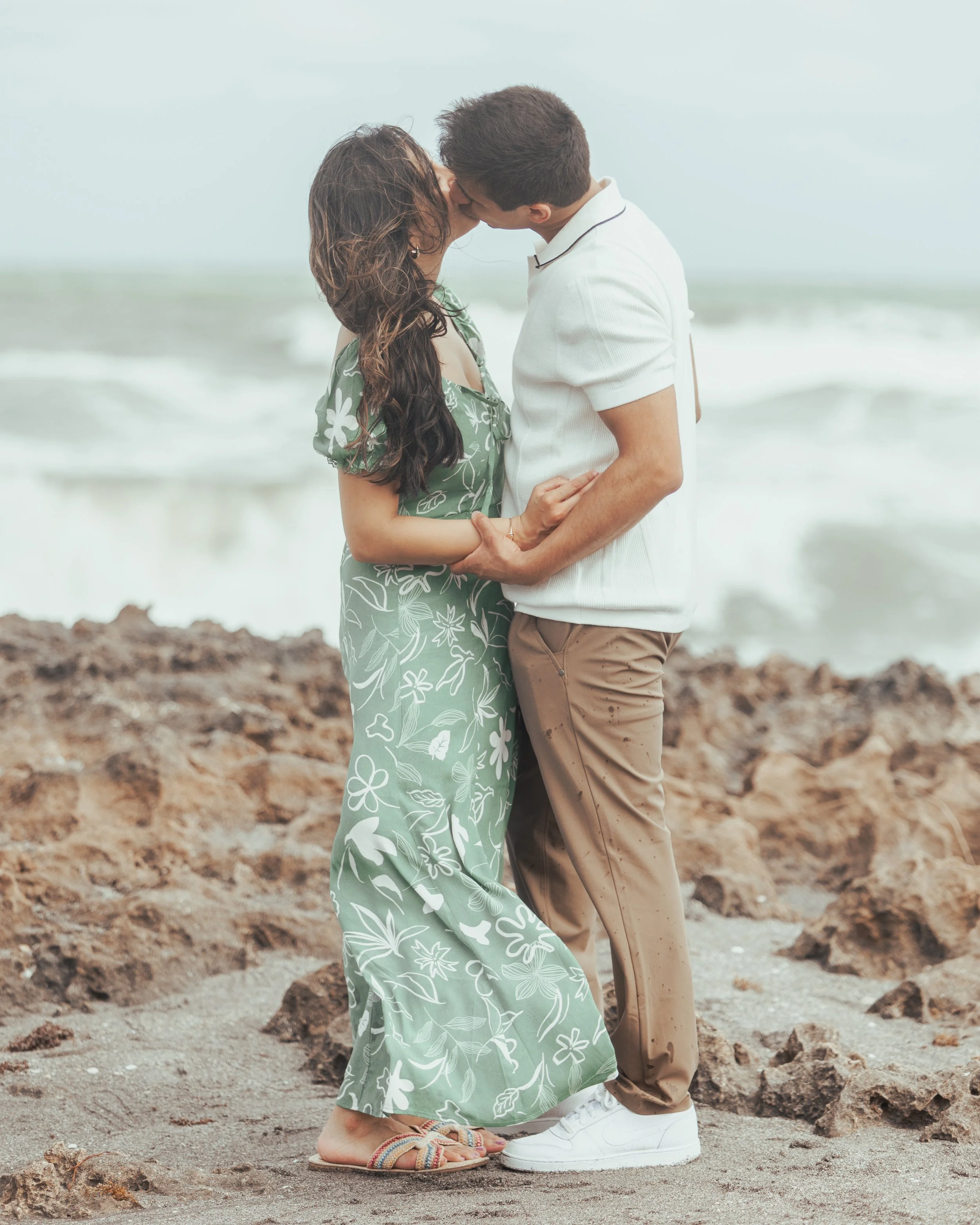 A couple kissing on a rocky beach, embracing each other.