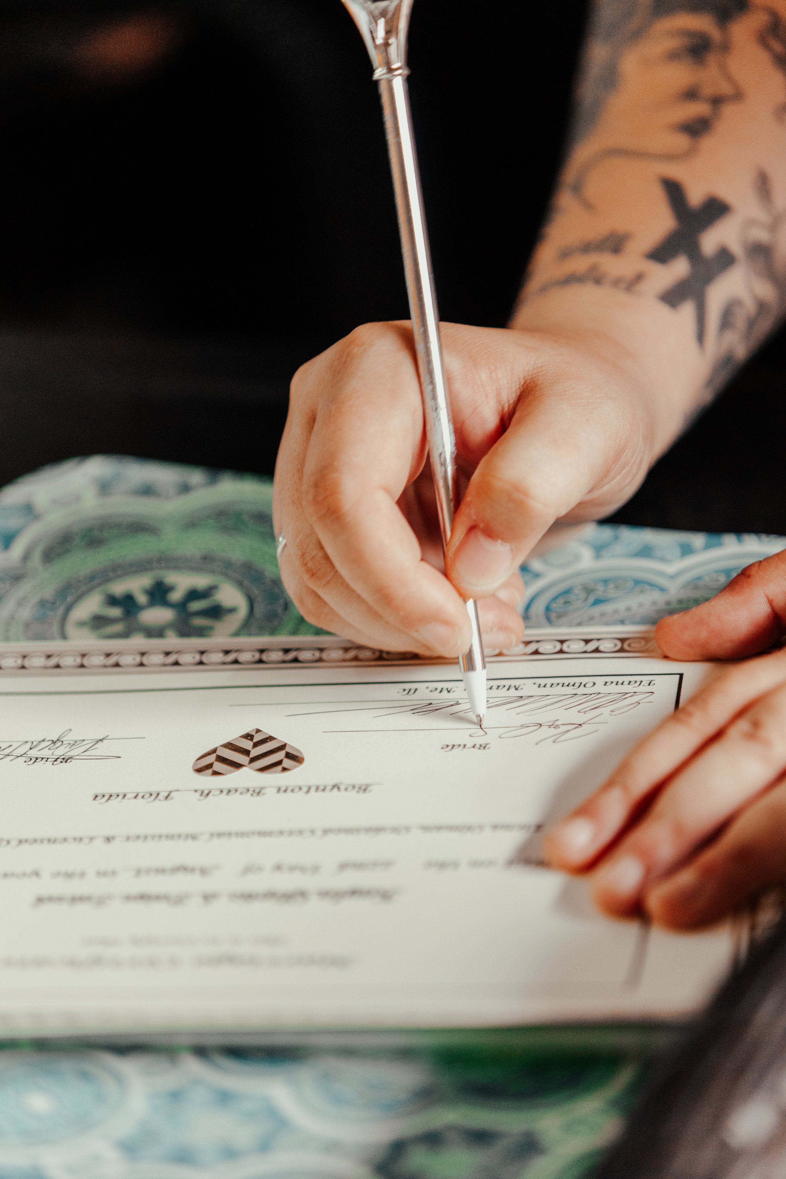 A person with tattoos signing a document, possibly a marriage certificate, with a pen.