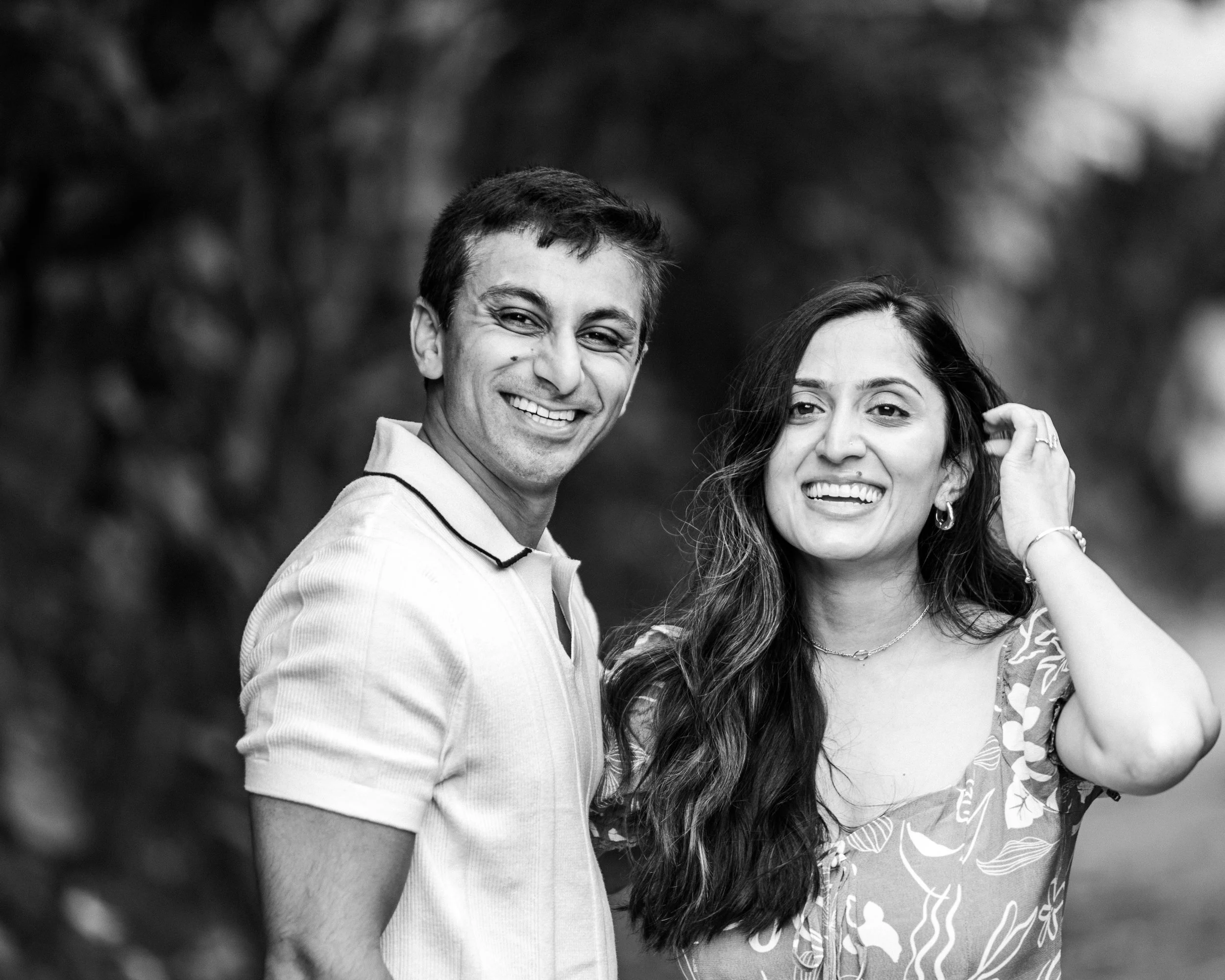A man and woman smiling outdoors with a blurred nature background.