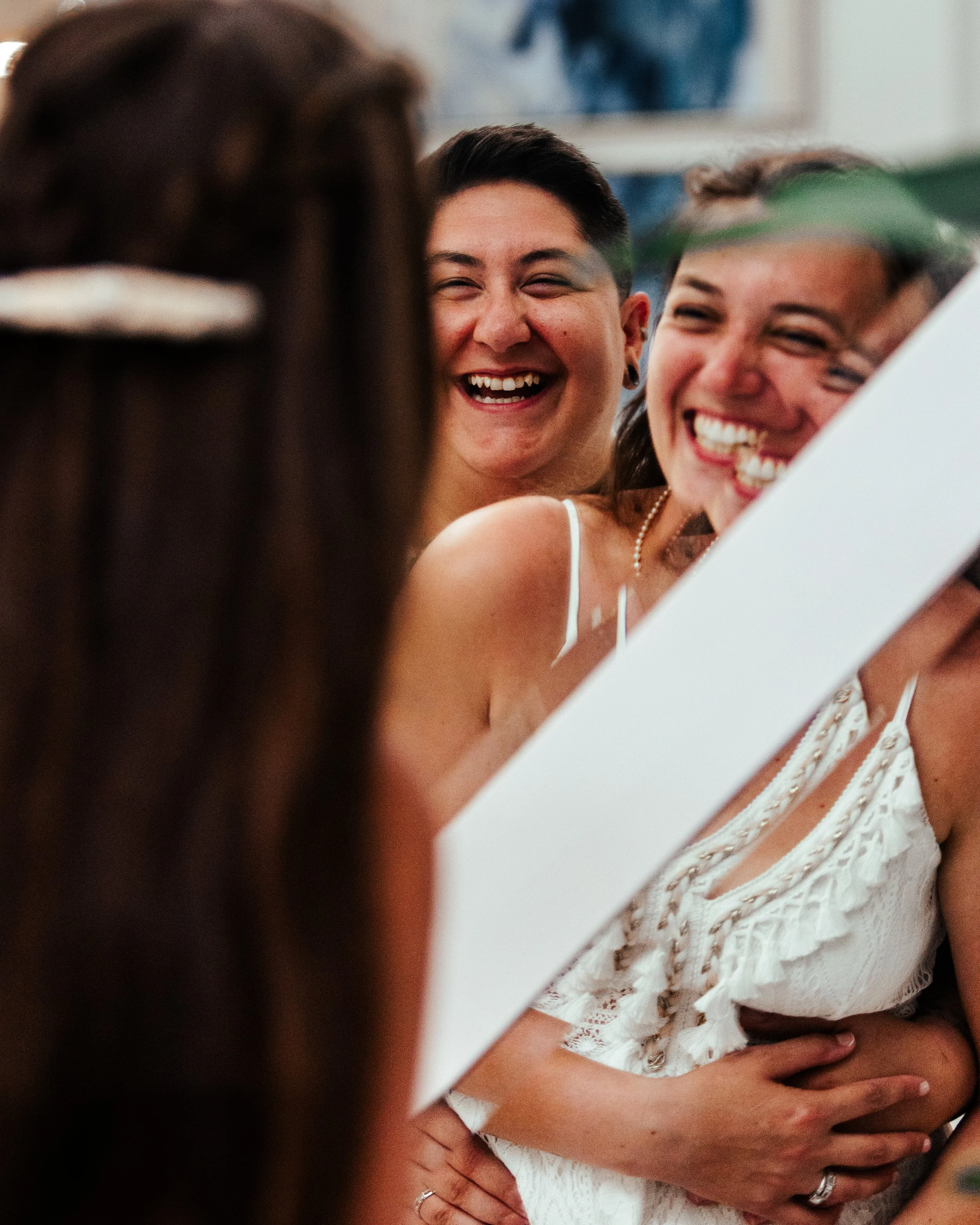 People smiling and laughing while looking at their reflection in a mirror, dressed in white, in a joyful moment.