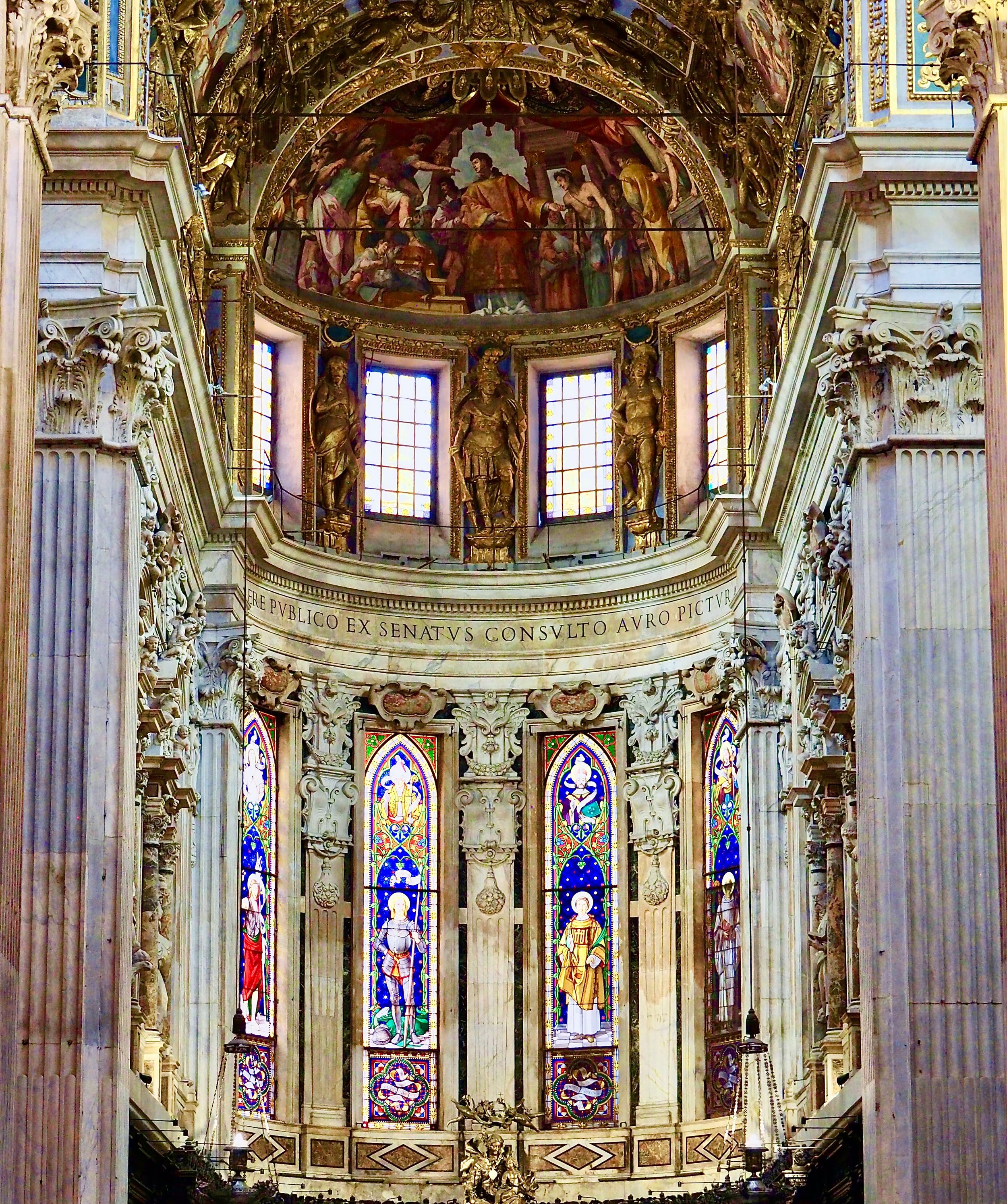 Interior of a church with stained glass windows depicting saints, ornate columns, and a frescoed dome ceiling.