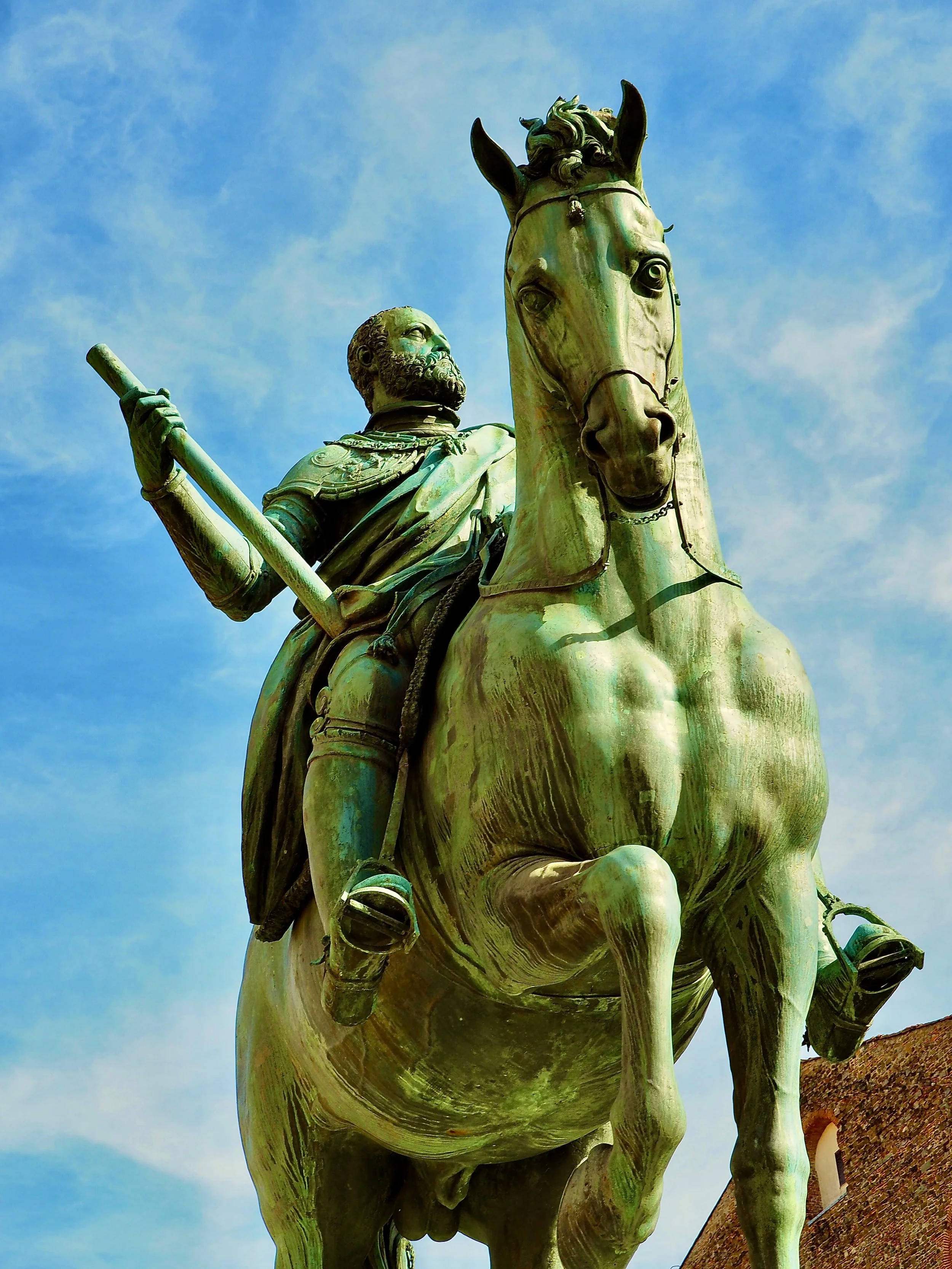Bronze statue of a man in armor sitting on a horse against a blue sky.