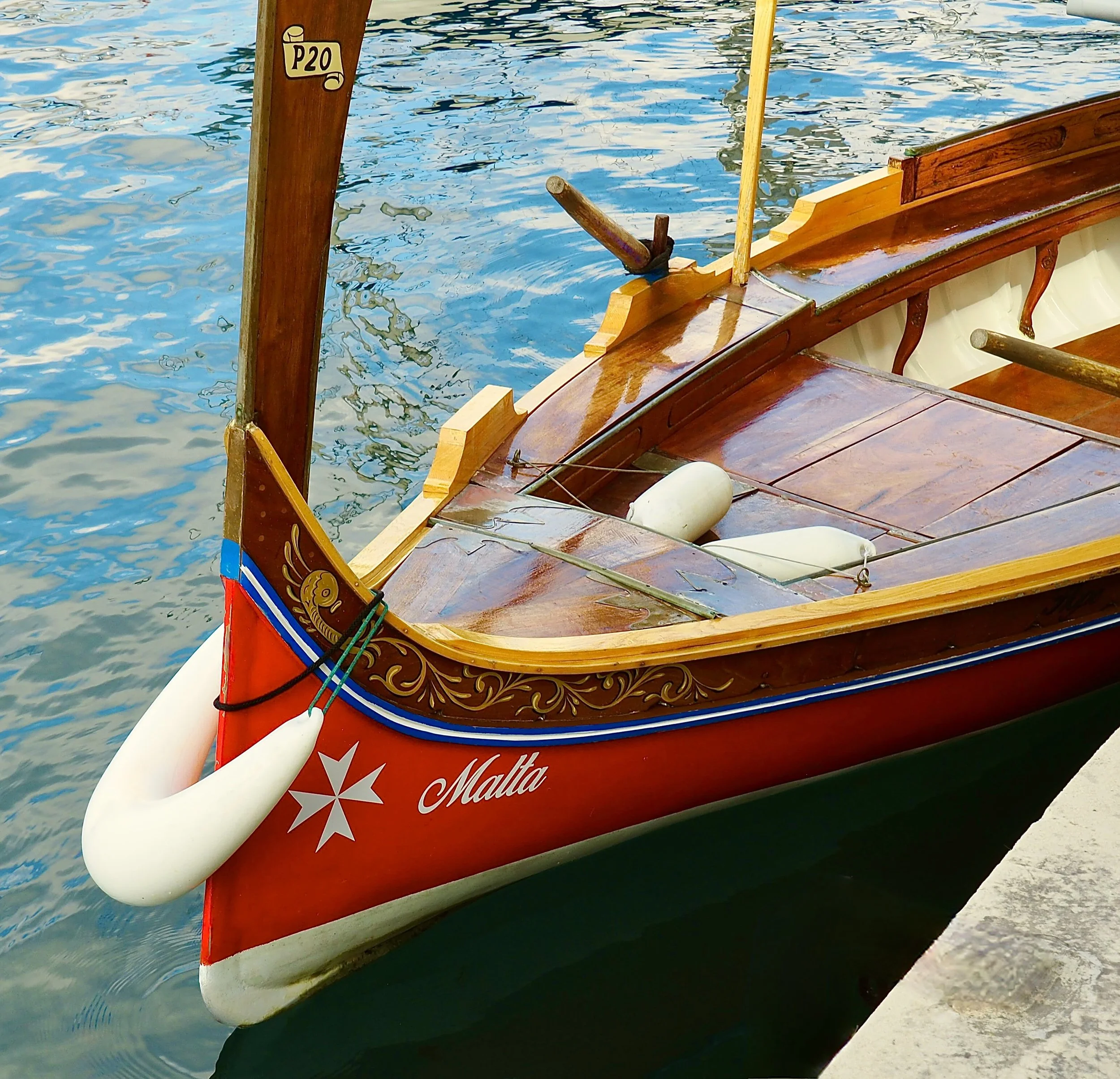 Close-up of a traditional wooden boat named Malta, docked by the water, with white fenders attached to its side.