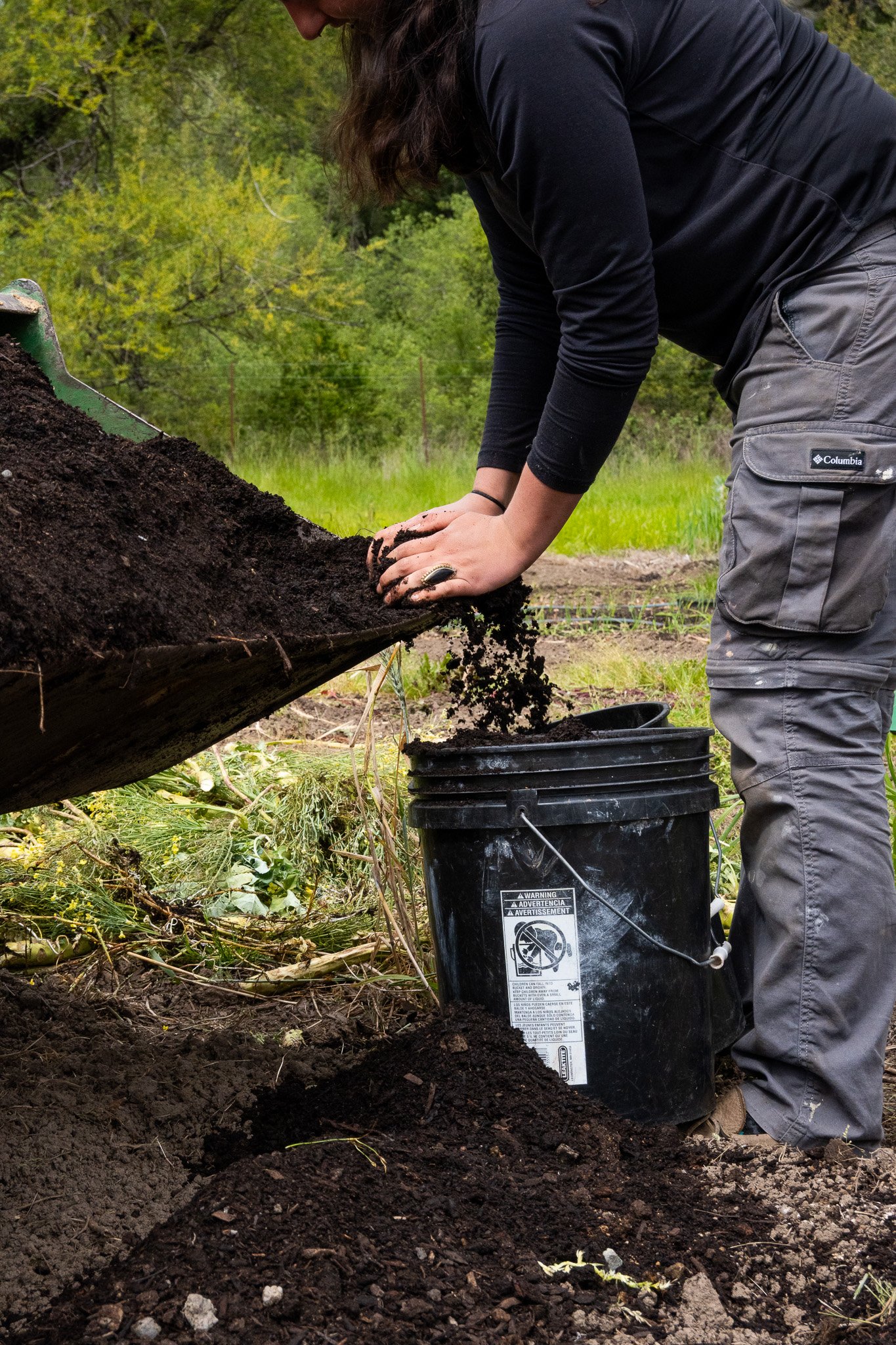 A farmer gathers compost into a bucket