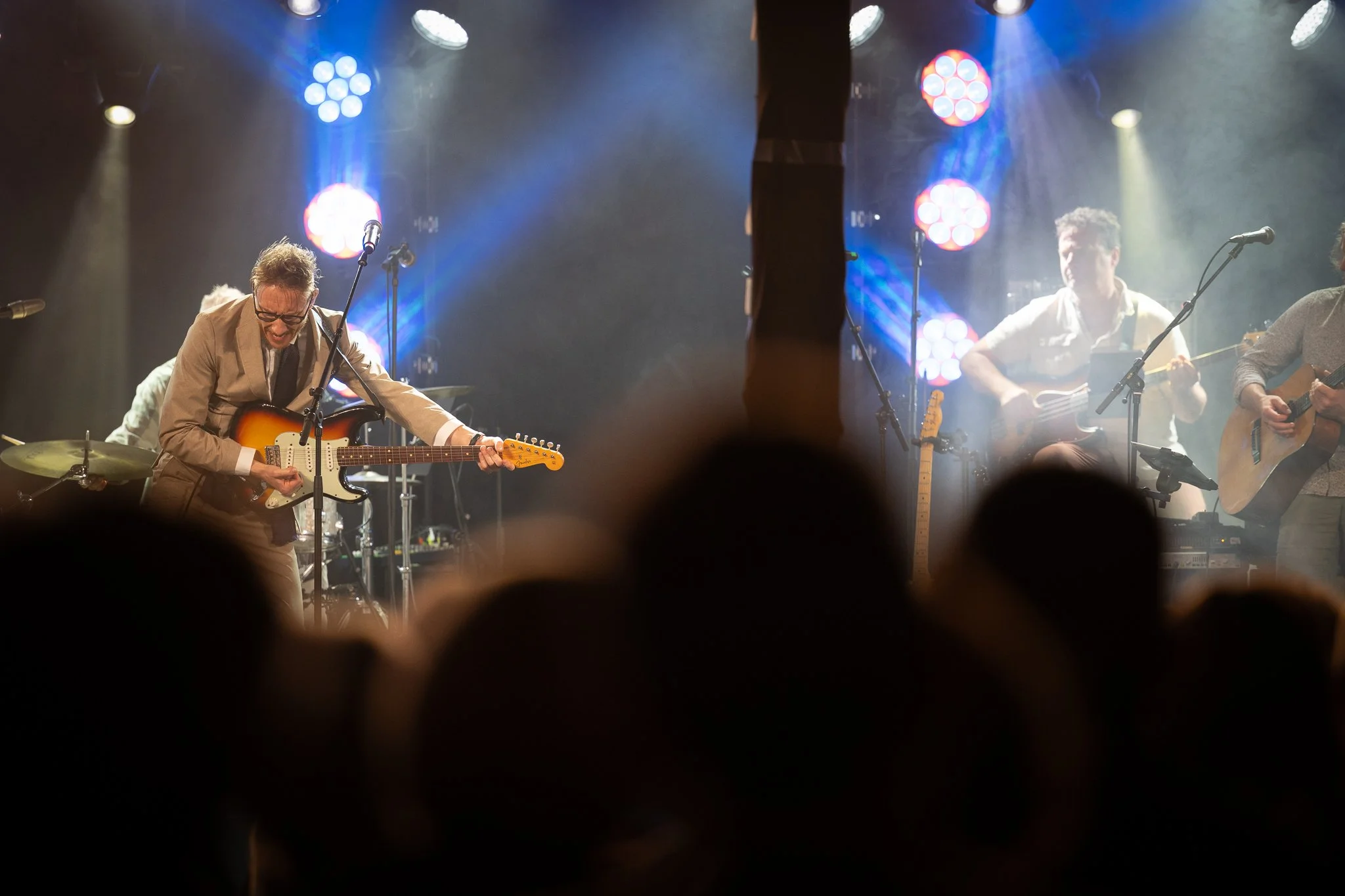 Adam Douglas. Et band på scenen som spiller gitar og synger, omgitt av scenelys og et publikum i forgrunnen.