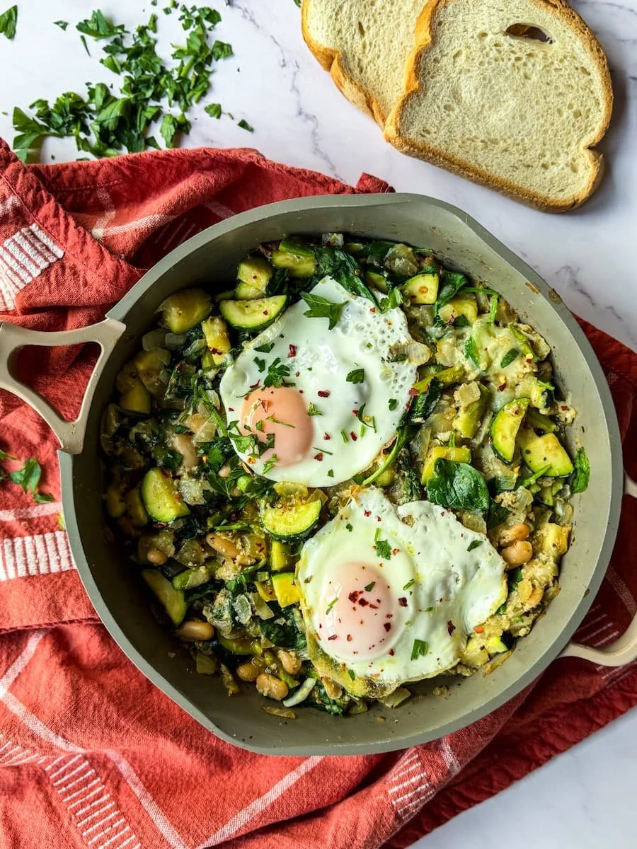 over easy eggs - overhead photo of pesto shakshuka in a pan with toasted bread next to it