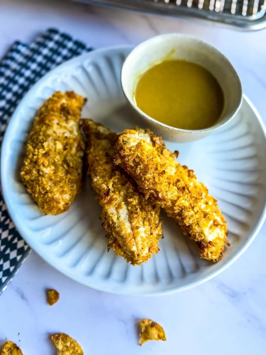 3 baked chicken tenders on a plate with honey mustard sauce on the side