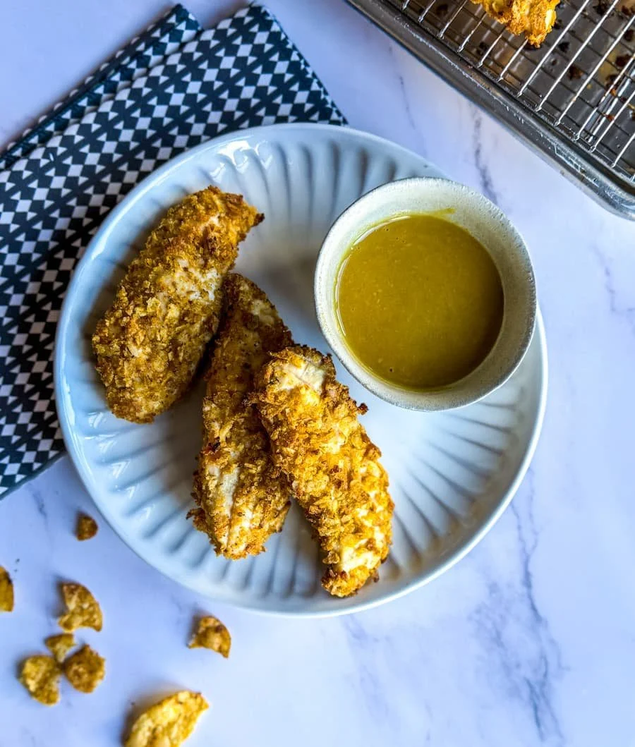 baked chicken tenders on a plate with a dish of honey mustard sauce