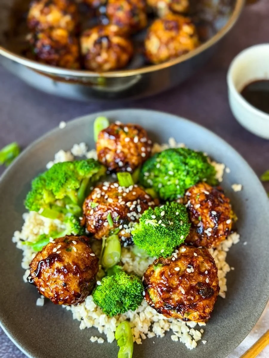 portion of turkey meatballs on a plate with steamed broccoli and rice with pan of glazed meatballs in the background