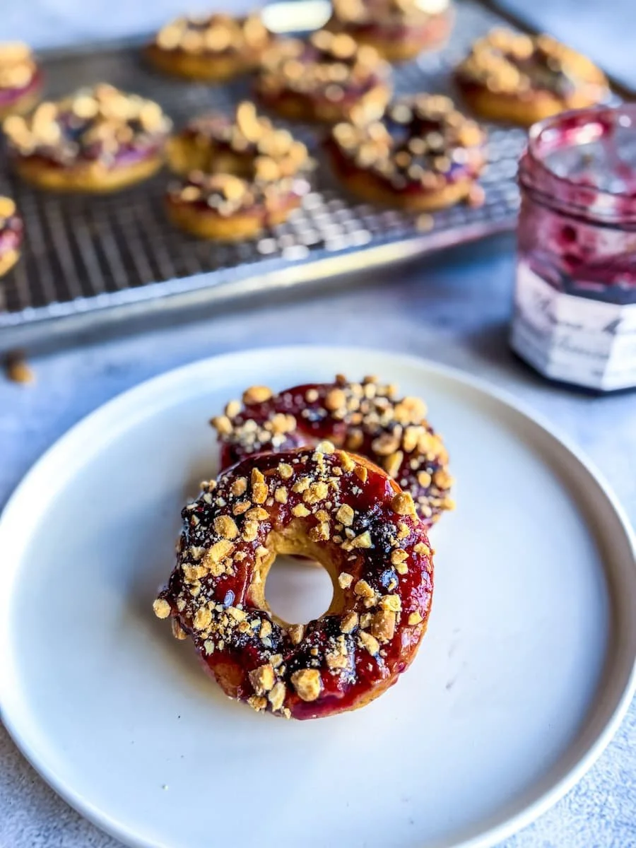 cake donut - two pb&j cake donuts on a plate in the foreground, more donuts on a wire rack in the background