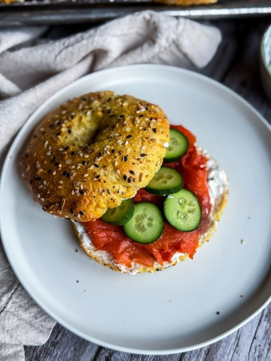 close-up photo of protein bagel on a plate with cream cheese, lox, and cucumber on one half / protein bagels