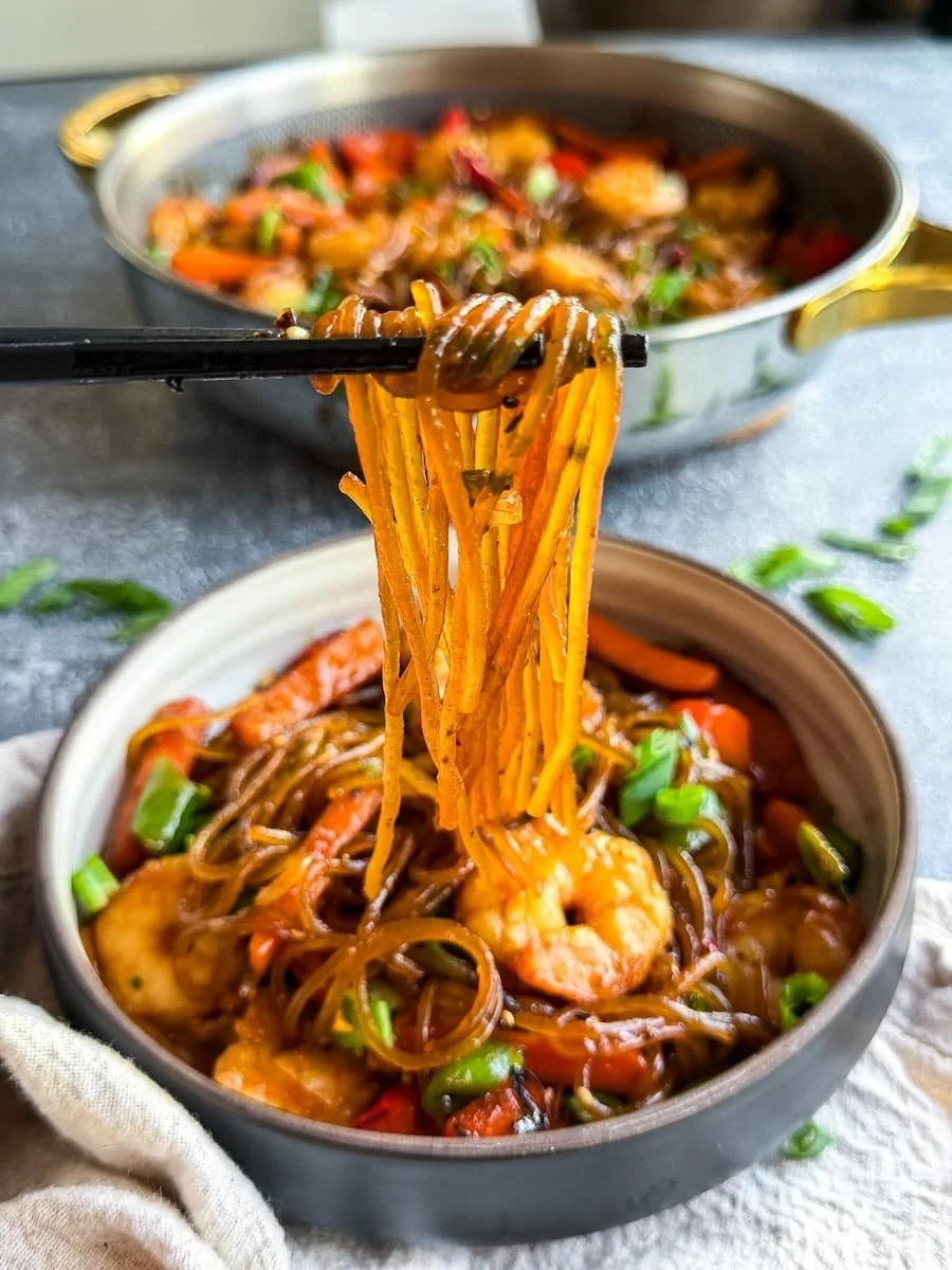 bowl of shrimp lo mein with chopsticks pulling noodles out of the bowl