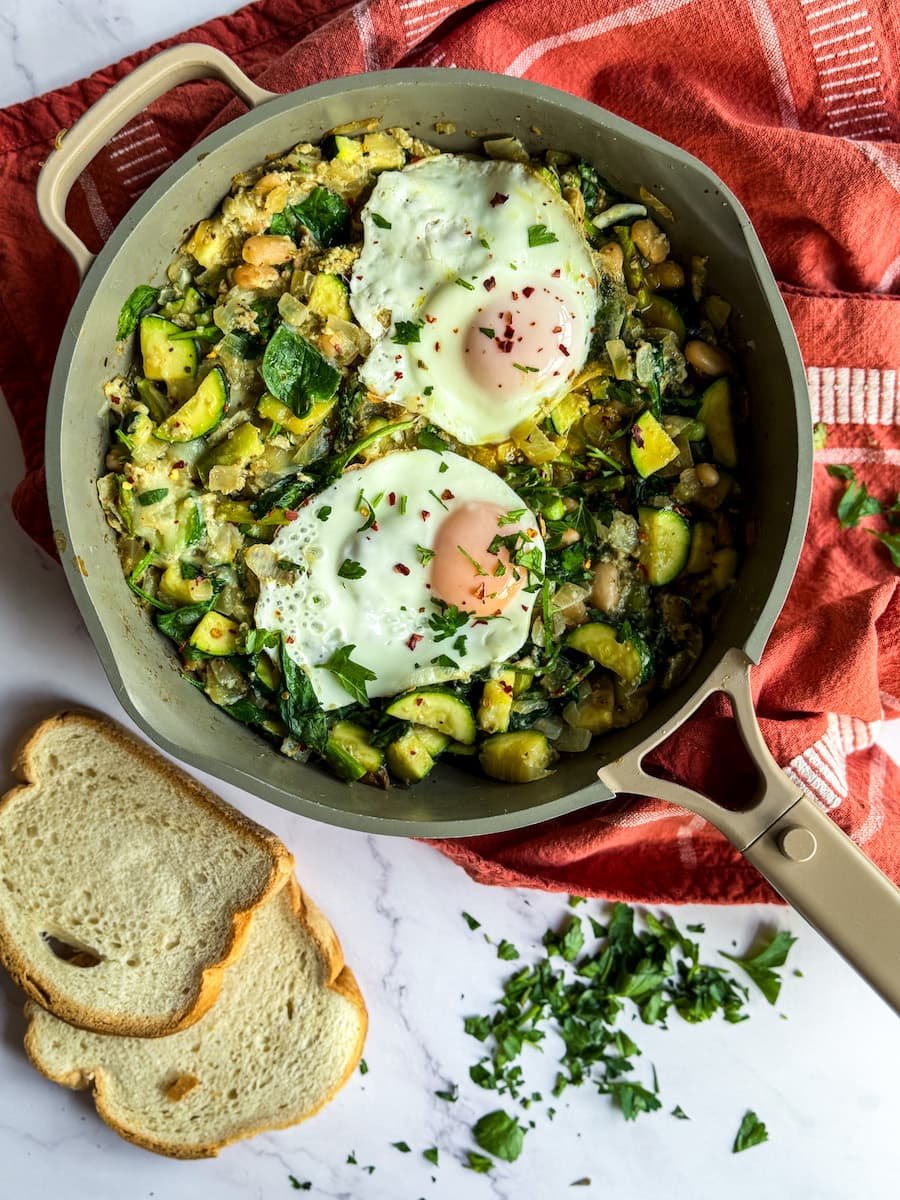 over easy eggs - eggs over the green shakshuka veggie base with toasted bread on the side
