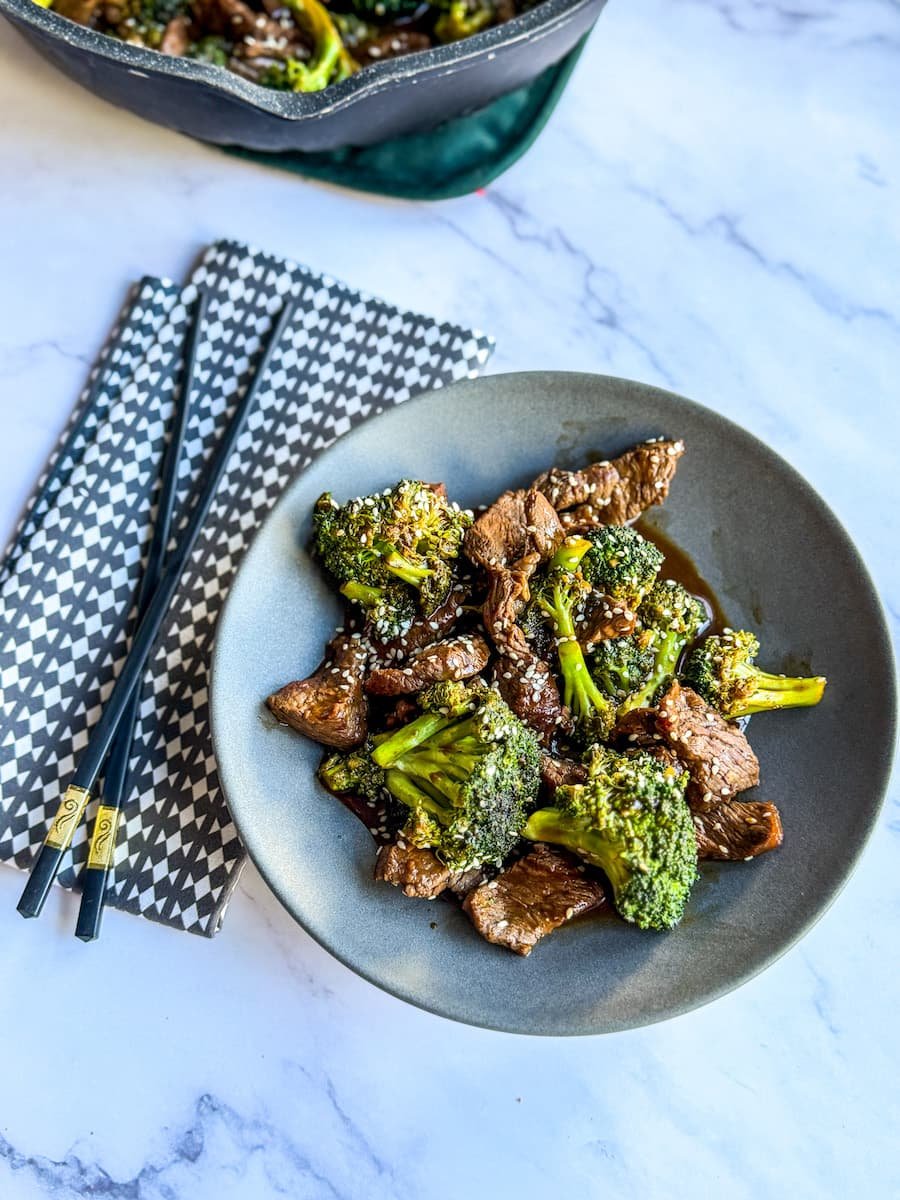 close-up of beef broccoli recipe on a plate with chopsticks and a cloth napkin next to it