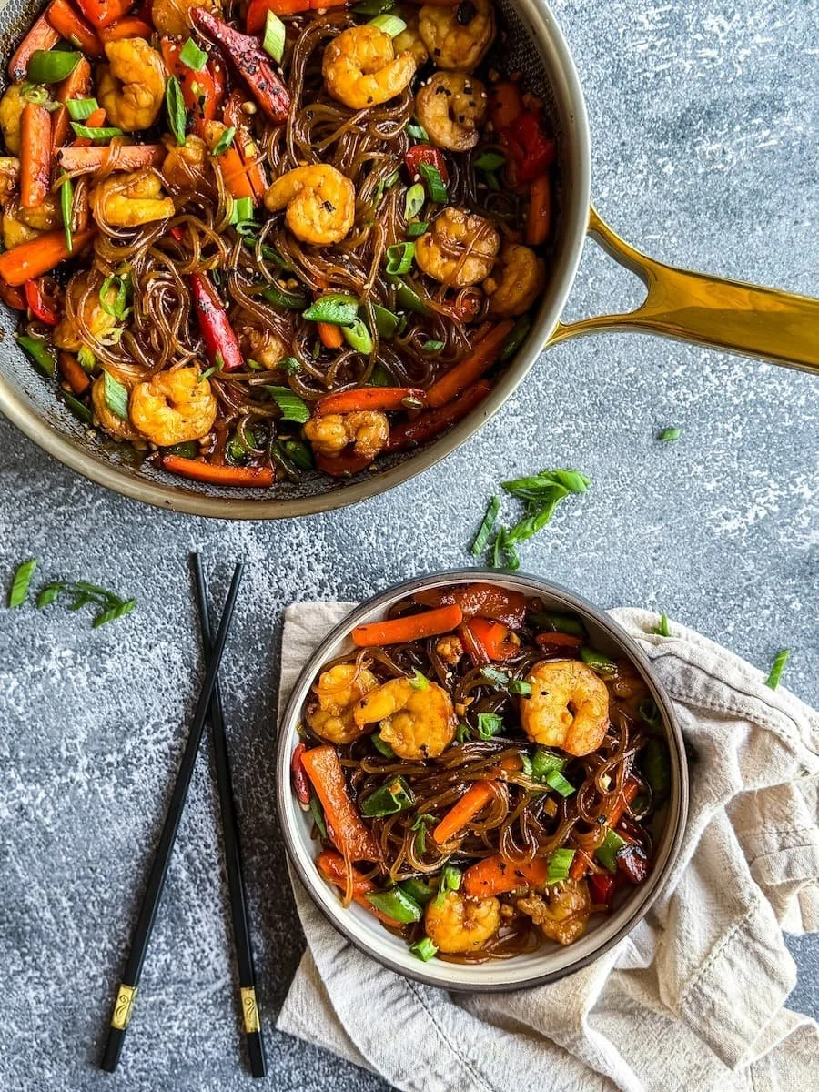 overhead photo of shrimp lo mein with a portion in a bowl with chopsticks next to it