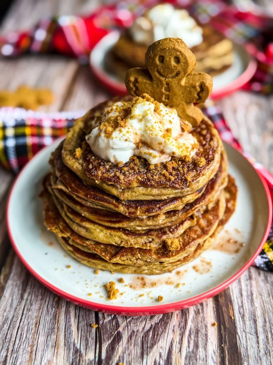 gingerbread protein pancakes / protein pancake recipe - a stack of pancakes on a plate topped with a mini gingerbread cookie, cookie crumbs, and a bit of yogurt