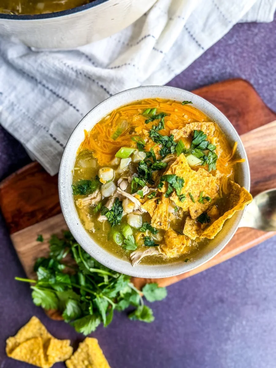 what is pozole / overhead shot of pozole verde garnished with tortilla chips, cheese, cilantro, and green onions