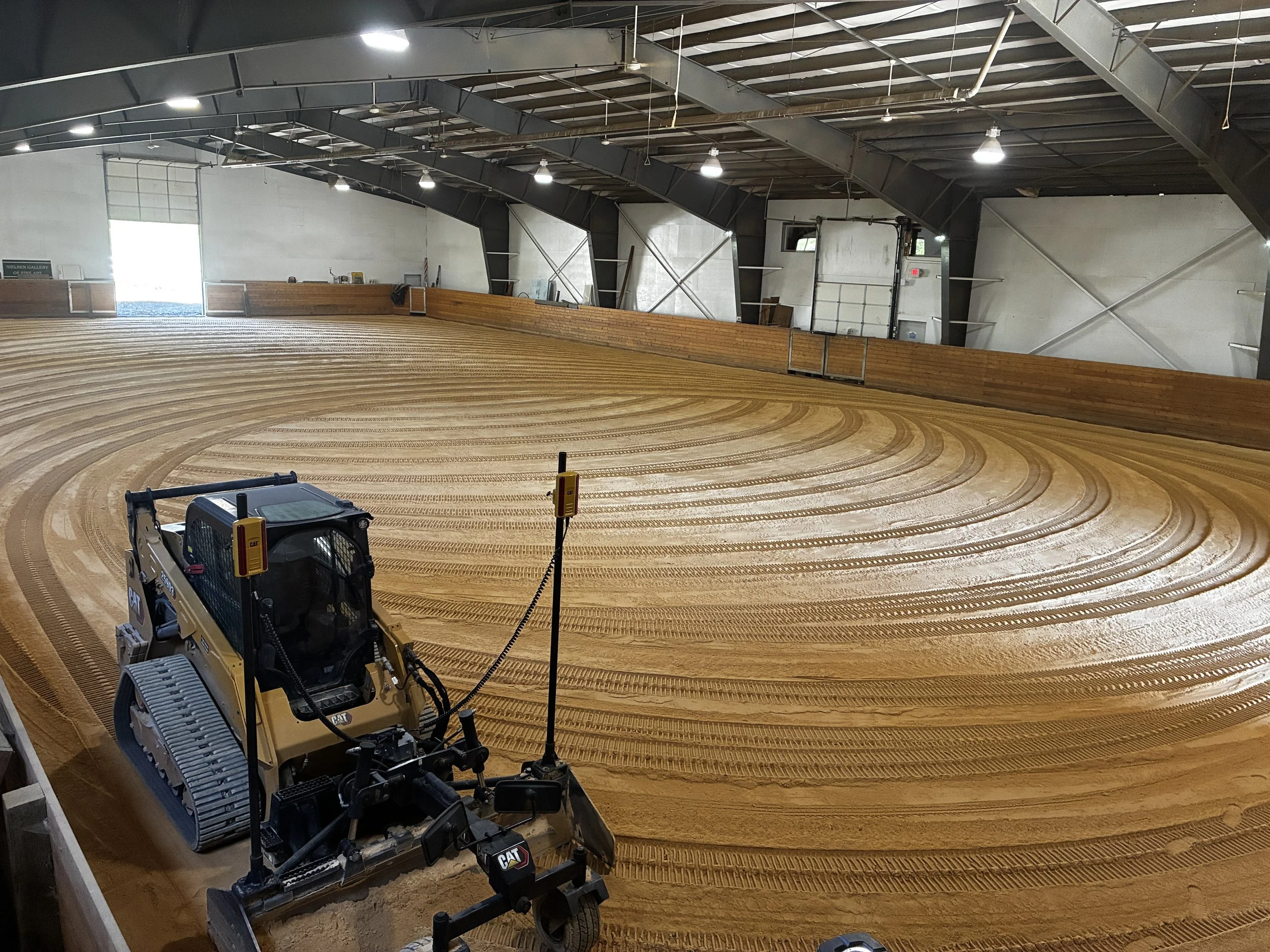 An indoor roller skating rink under construction with tracks of sand and a small Caterpillar bulldozer in the foreground.