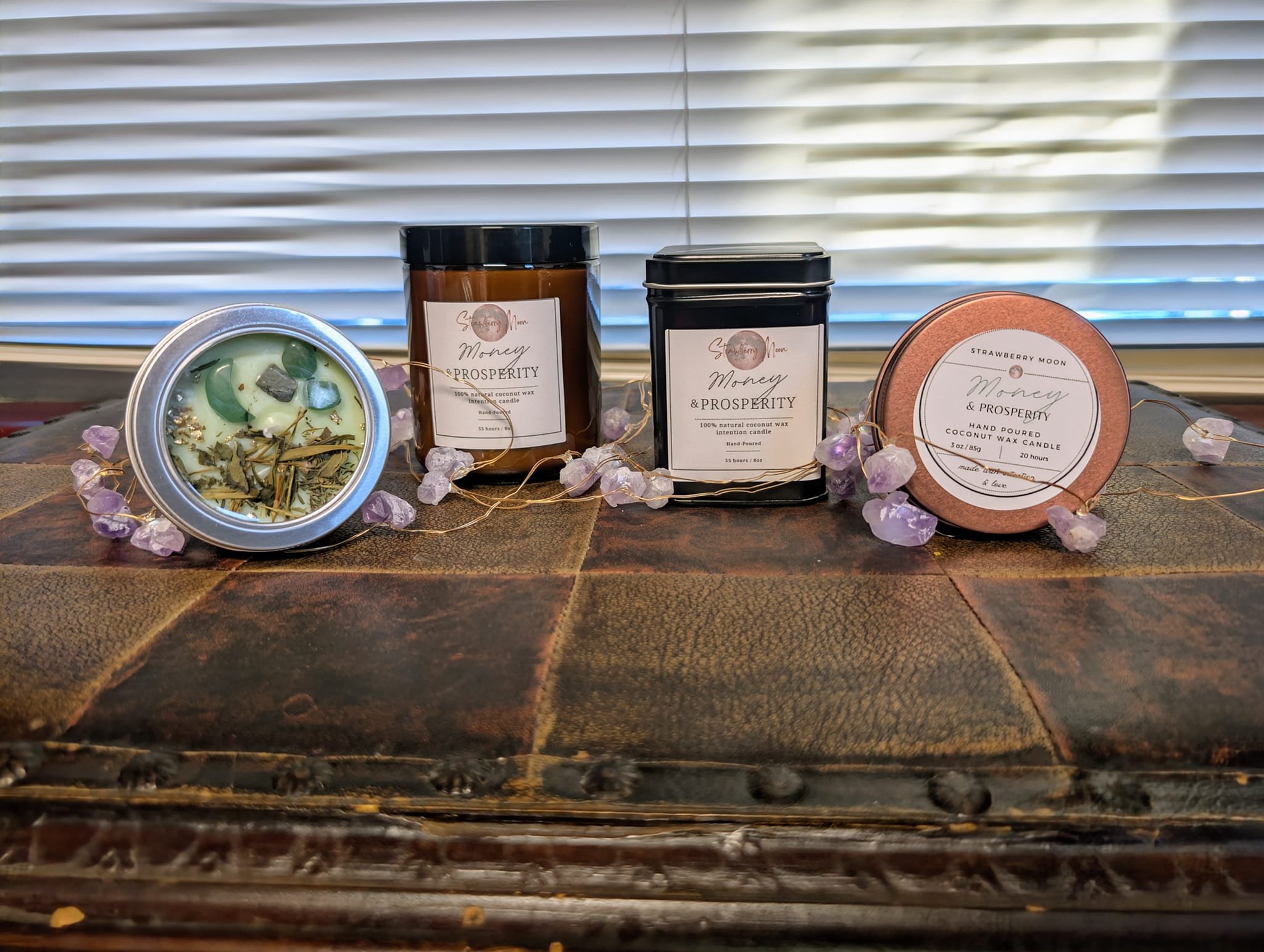 Collection of scented candles with labels and decorative stones on a wooden surface with a window in the background.