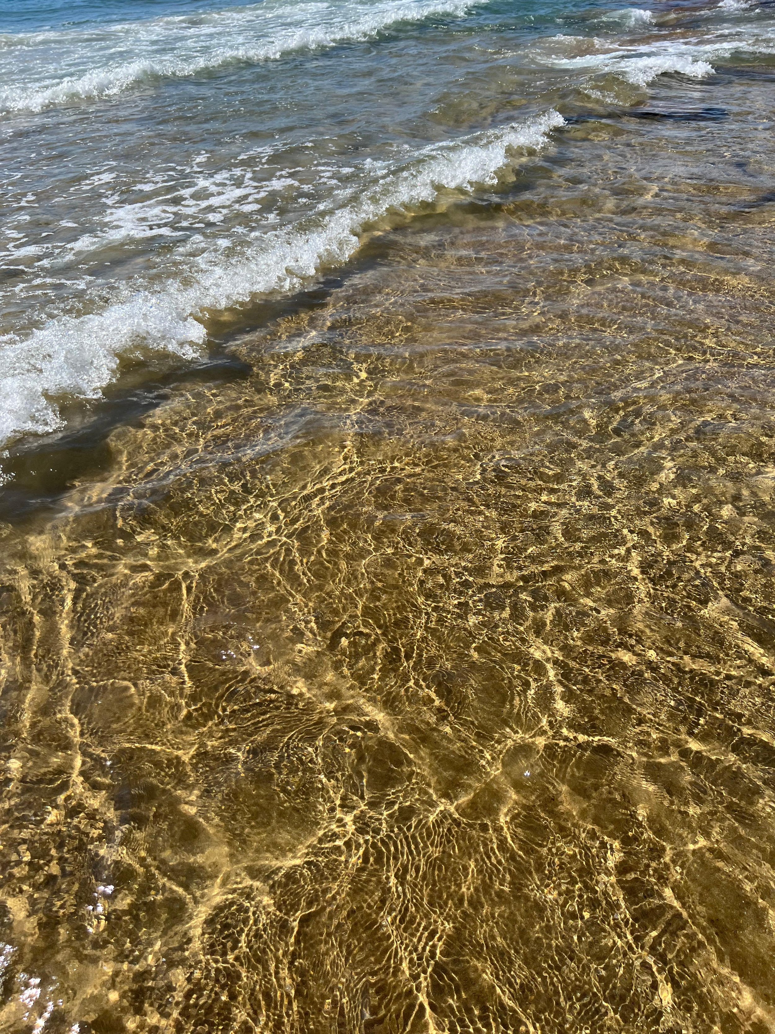 Spiaggia con onde che si infrangono su sabbia dorata e acqua trasparente.