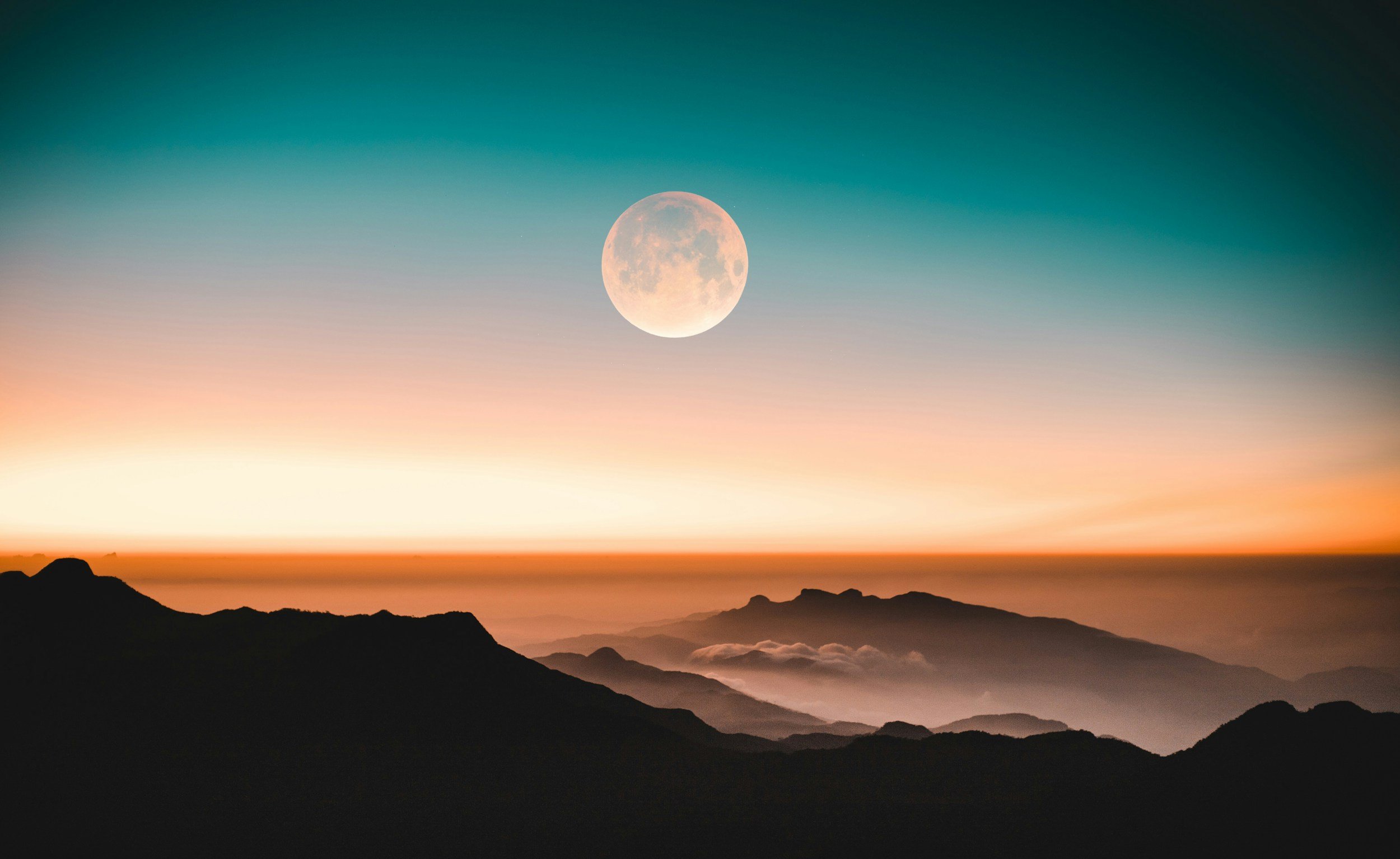A scenic view of mountains at dusk with a colorful sky and a large, bright full moon above the horizon.