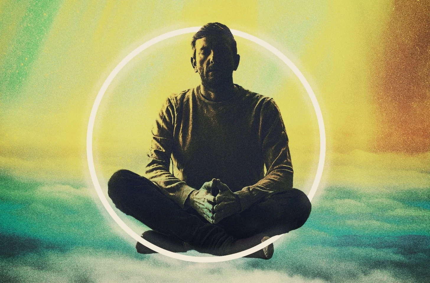 Silhouette of a man sitting cross-legged with hands clasped, surrounded by a glowing circular light, against a multicolored background.