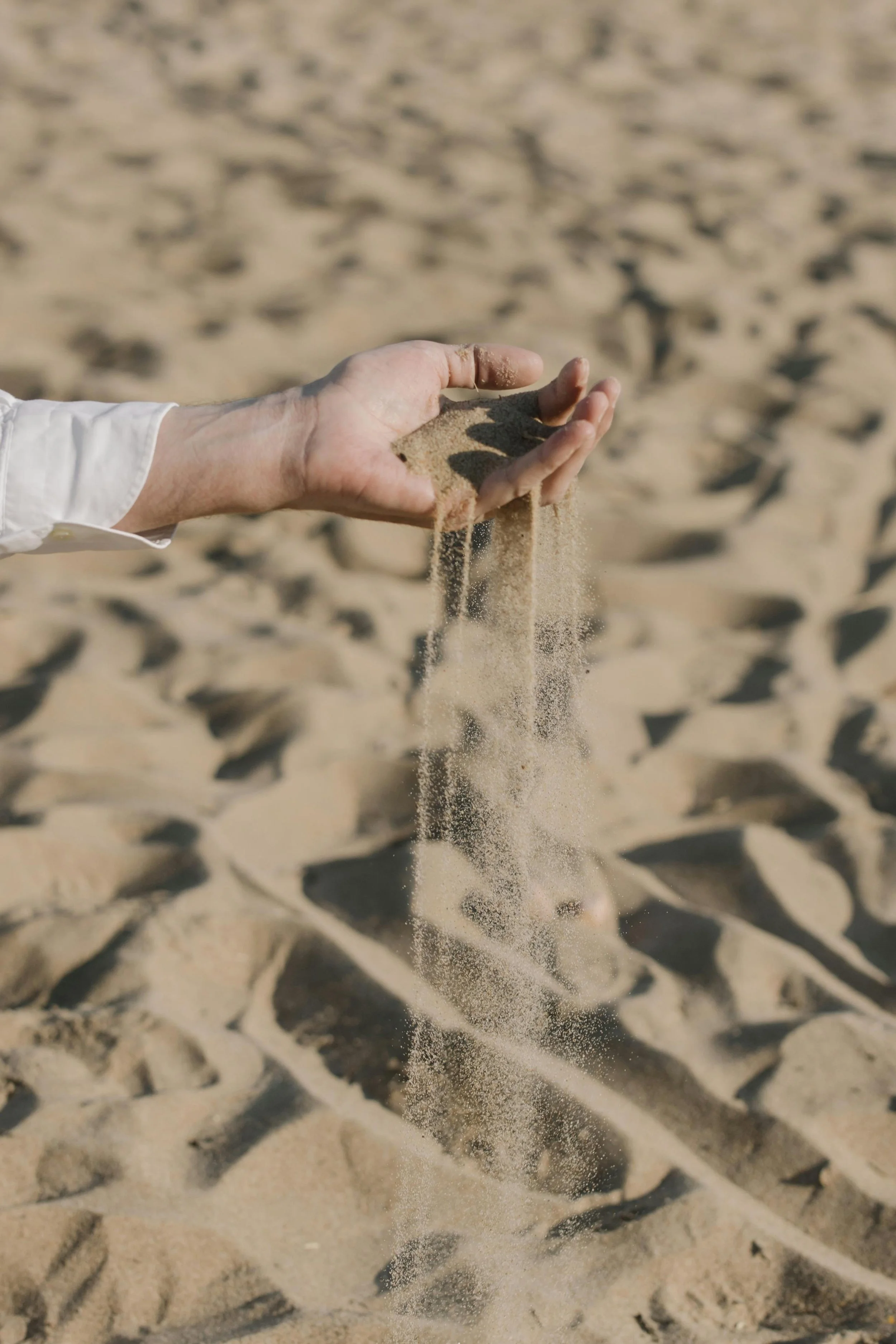 Hand holding sand on a beach, with sand falling through fingers.