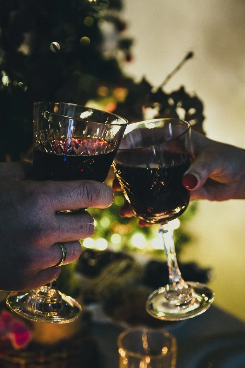 Rødvinsglas ved julefrokost - To personer skåler med rødvin ved et juletræ.