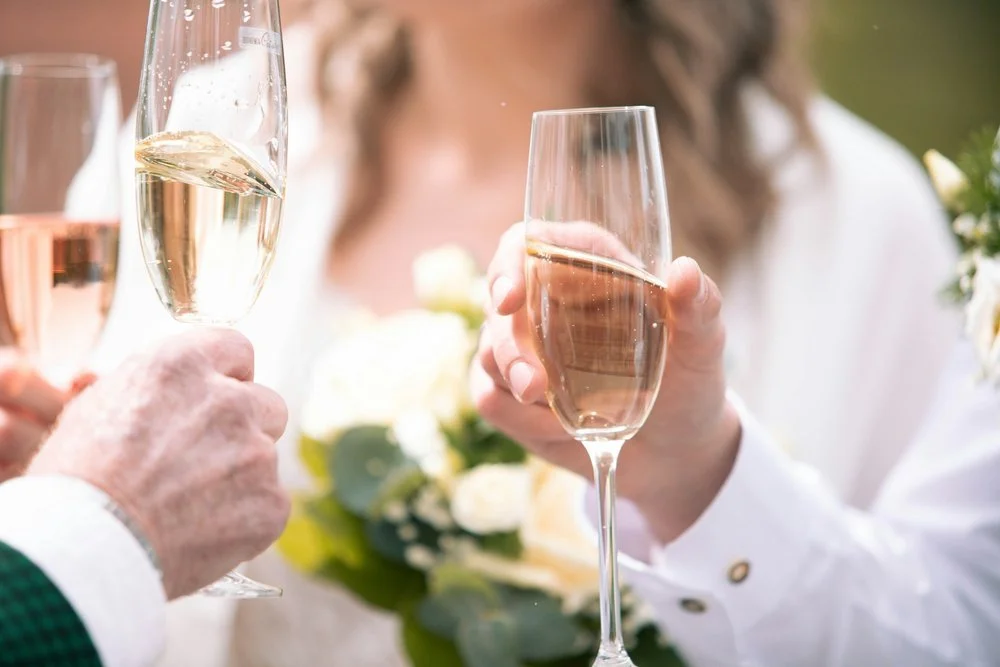 Glas sprudlende champagne til velkomst - To personer skåler med champagneglas under en festlig begivenhed.