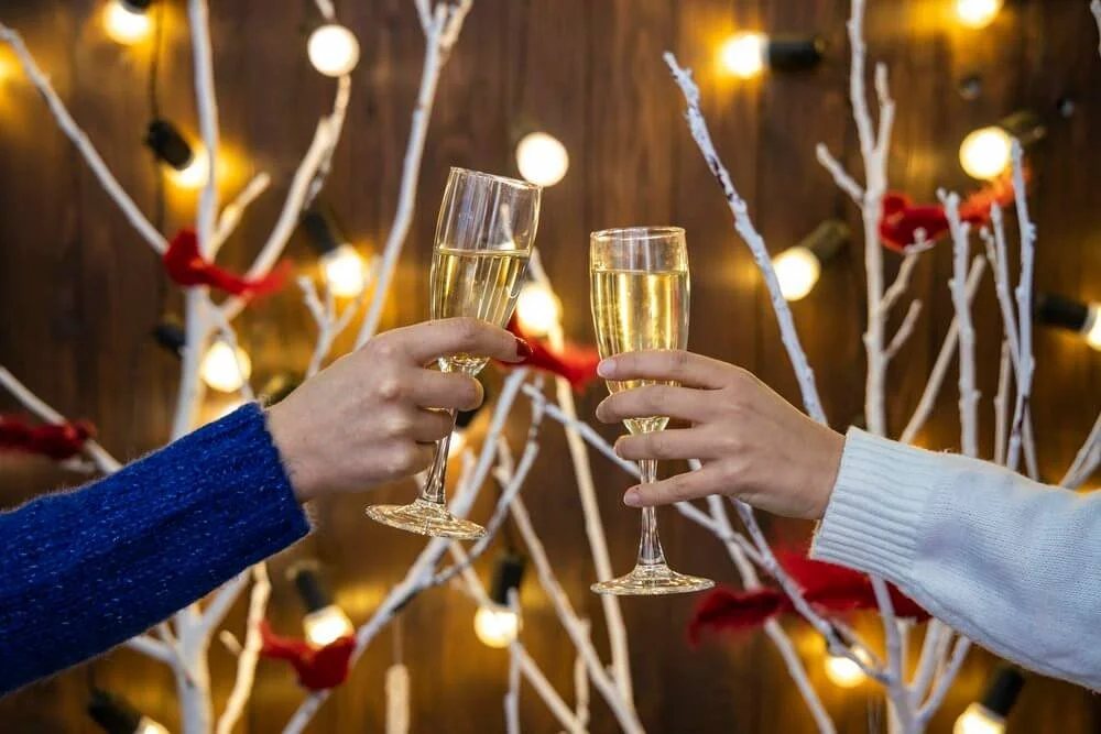 Champagneglas til skål ved julefrokost - To personer skåler med champagneglas til en julefrokost med dekorationer i baggrunden.