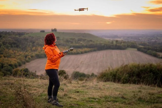 Woman flying a drone outdoors during sunset.