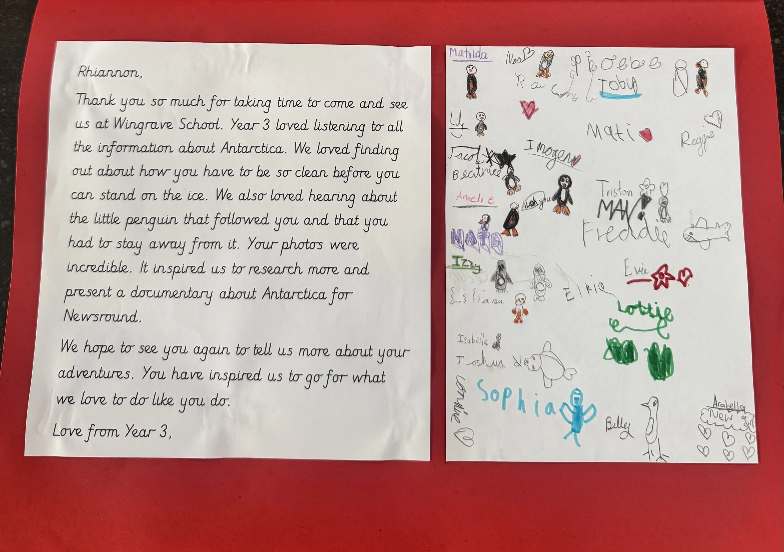 A handwritten letter on white paper with colorful children's drawings and signatures, placed on a red background.