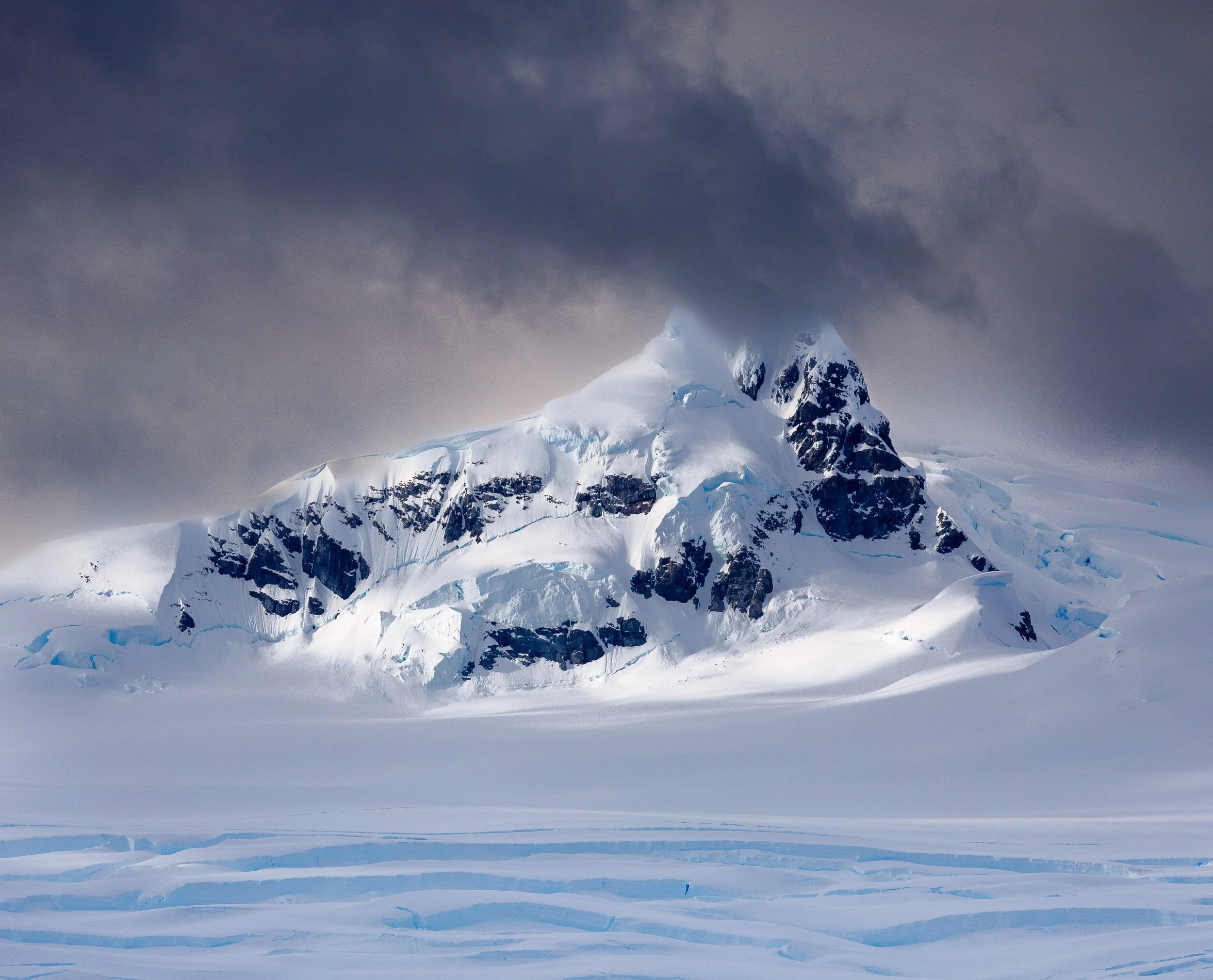 Snow-covered mountain in Antarctica with dark clouds above