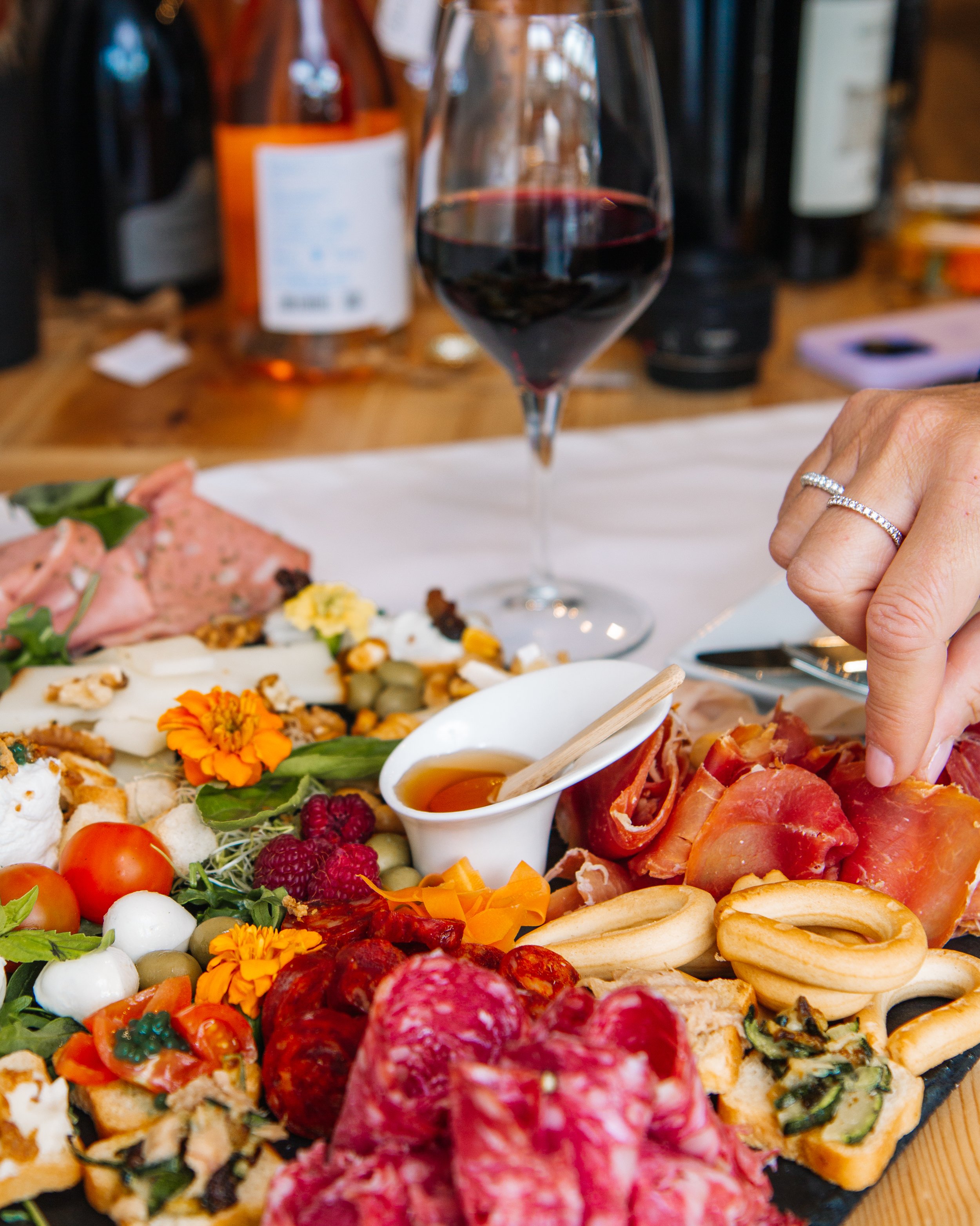 Exquisita selección de embutidos y quesos, perfectamente acompañada de una copa de vino tinto, presentada en una mesa de madera que resalta la frescura y calidad de los ingredientes, ideal para una velada gourmet